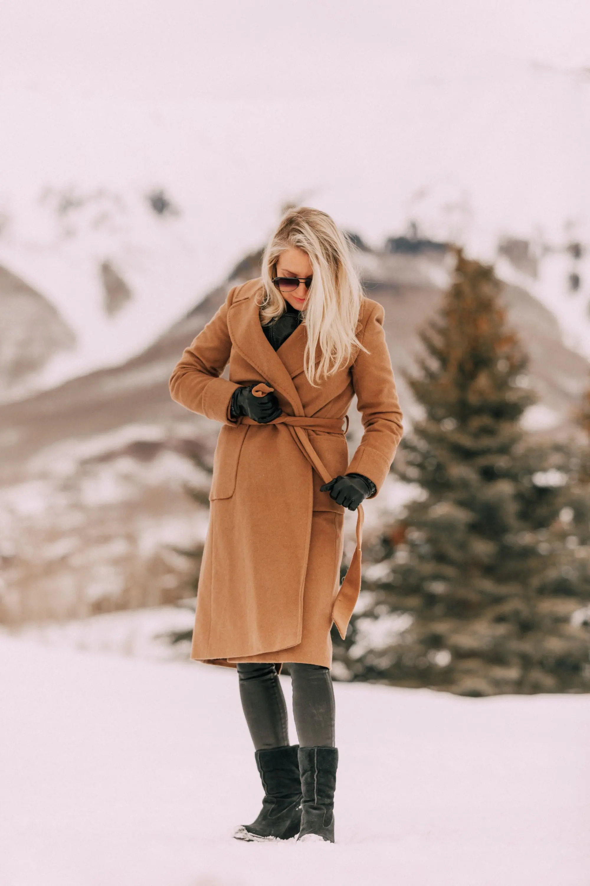 How To Layer A Moto Jacket, Fashion blogger wearing a black leather IRO moto jacket underneath Mackage long camel coat Carolina Amato gloves, rocket leatherette skinny jeans by Citizens of Humanity, black cashmere turtleneck, and Ugg wedge boots in Telluride, CO
