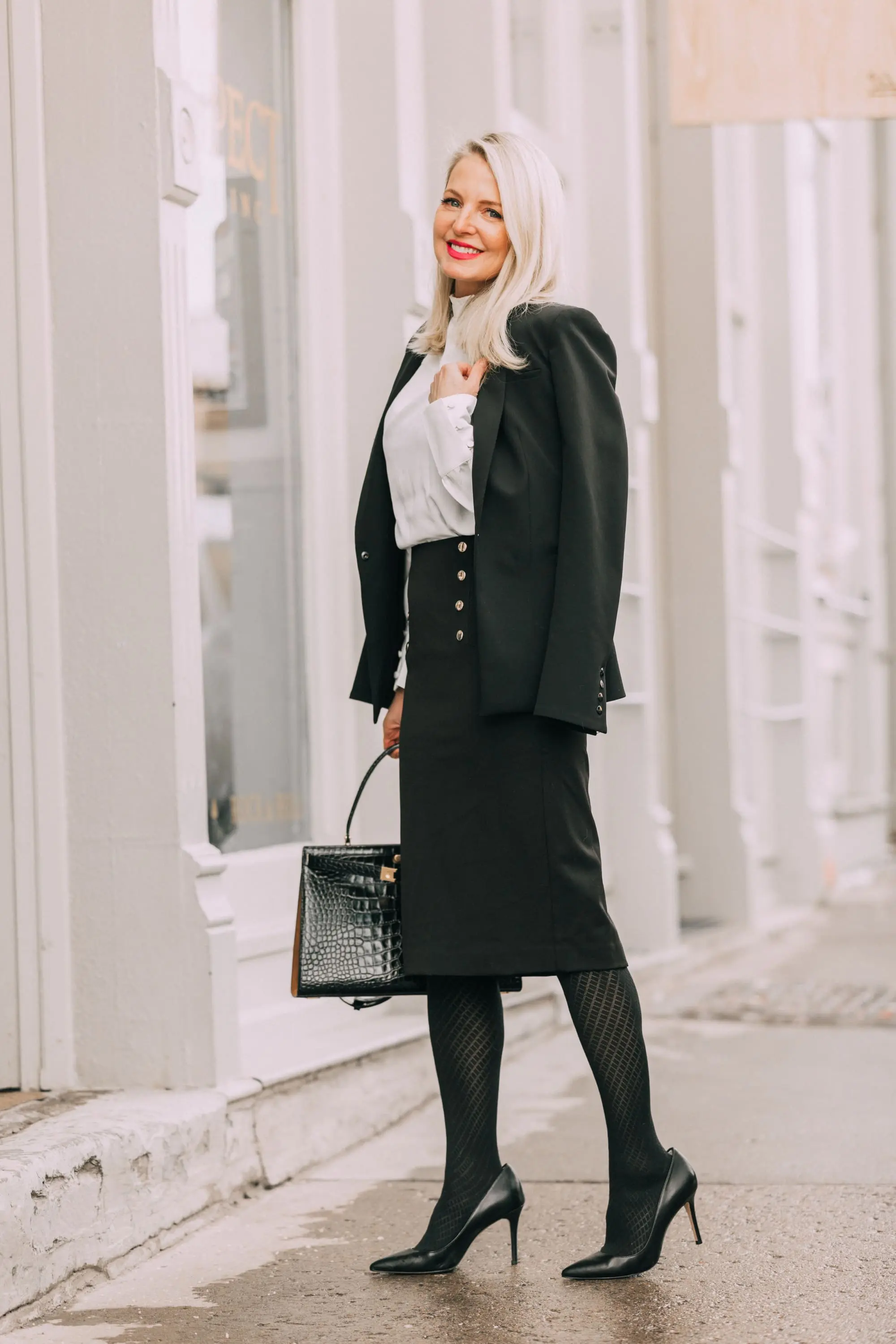 Wardrobe Basics, Fashion blogger Erin Busbee of BusbeeStyle.com sharing wardrobe basics from Ann Taylor wearing a black pencil skirt with sailir buttons, a white ruffle neck blouse, classic black blazer, black tights, and black pumps all from Ann Taylor in Telluride, Colorado