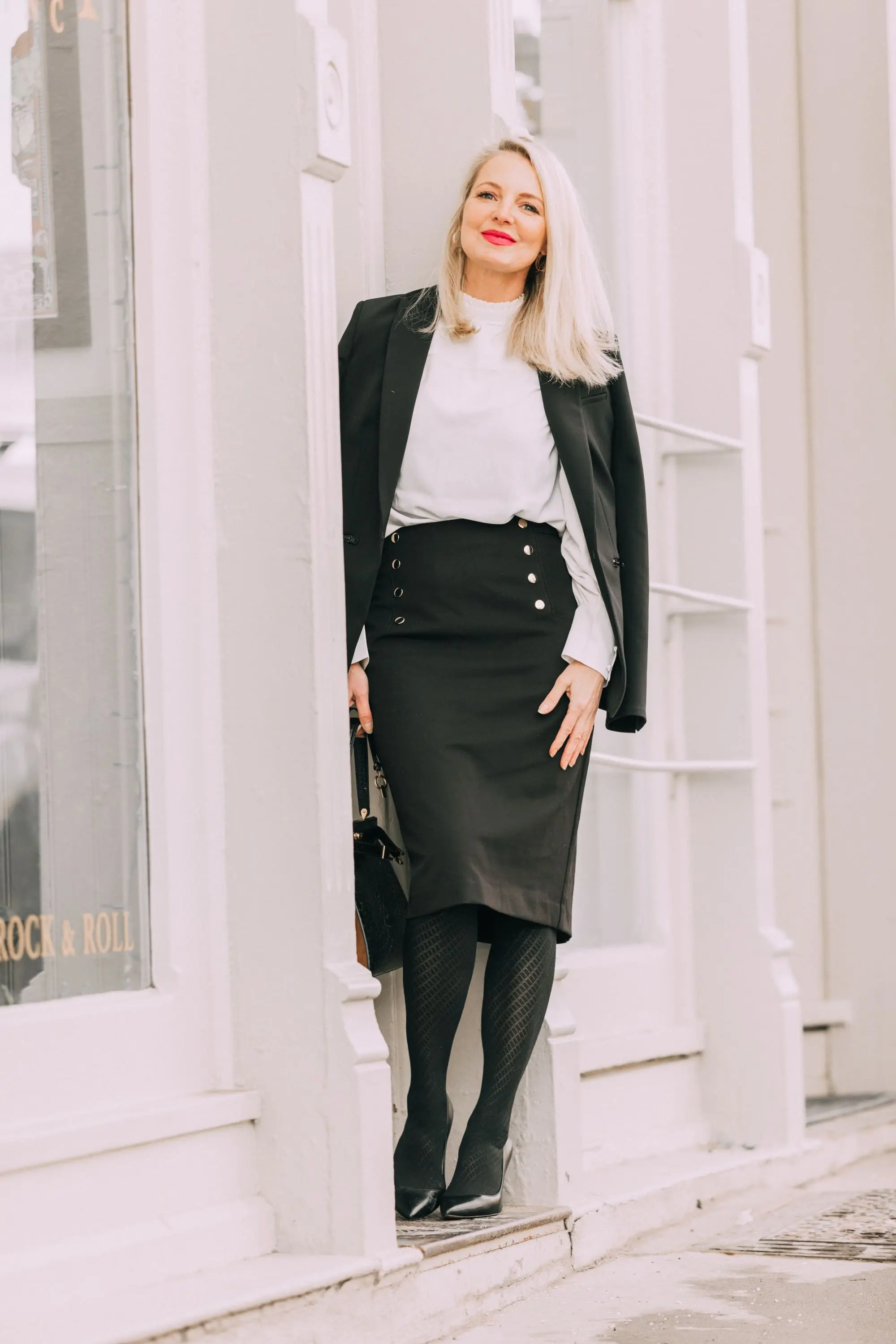 Wardrobe Basics, Fashion blogger Erin Busbee of BusbeeStyle.com sharing wardrobe basics from Ann Taylor wearing a black pencil skirt with sailir buttons, a white ruffle neck blouse, classic black blazer, black tights, and black pumps all from Ann Taylor in Telluride, Colorado