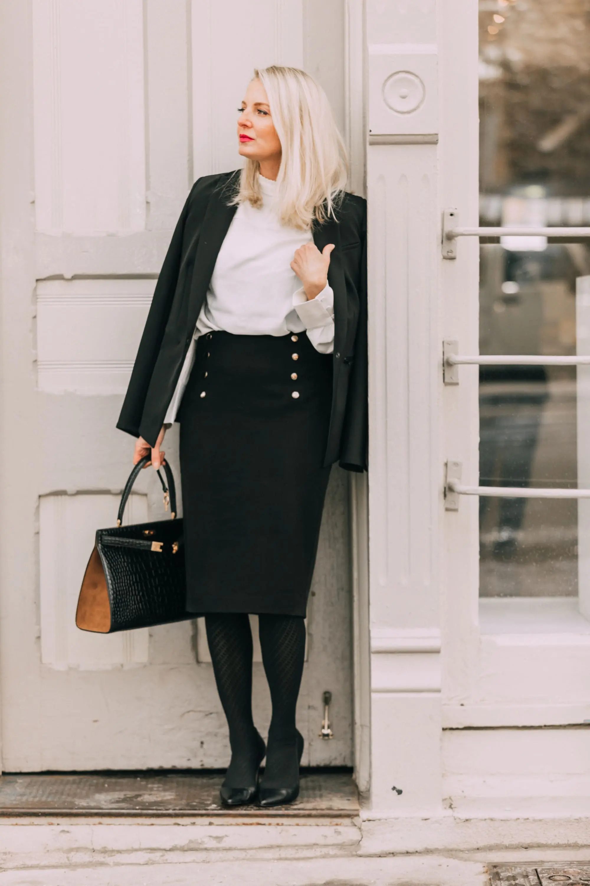 Wardrobe Basics, Fashion blogger Erin Busbee of BusbeeStyle.com sharing wardrobe basics from Ann Taylor wearing a black pencil skirt with sailir buttons, a white ruffle neck blouse, classic black blazer, black tights, and black pumps all from Ann Taylor in Telluride, Colorado