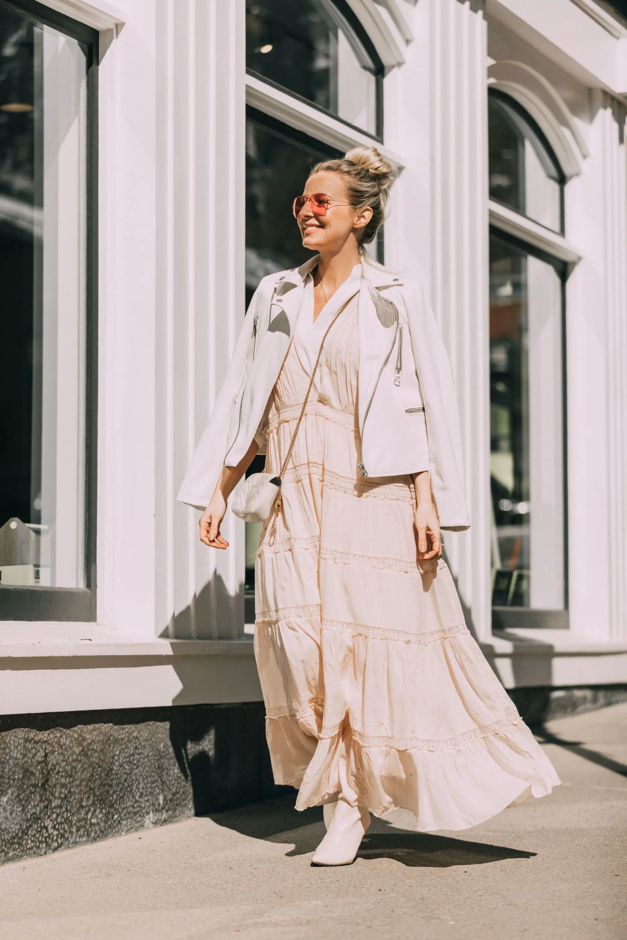 How To Wear A Maxi Dress, Fashion blogger Erin Busbee of BusbeeStyle.com wearing a peach Free People Lily of the Valley Maxi dress over a bubble sleeve white blouse by Frame, white cone heel booties, white crossbody bag, and white faux leather moto jacket from Scoop at Walmart walking in Telluride, Colorado