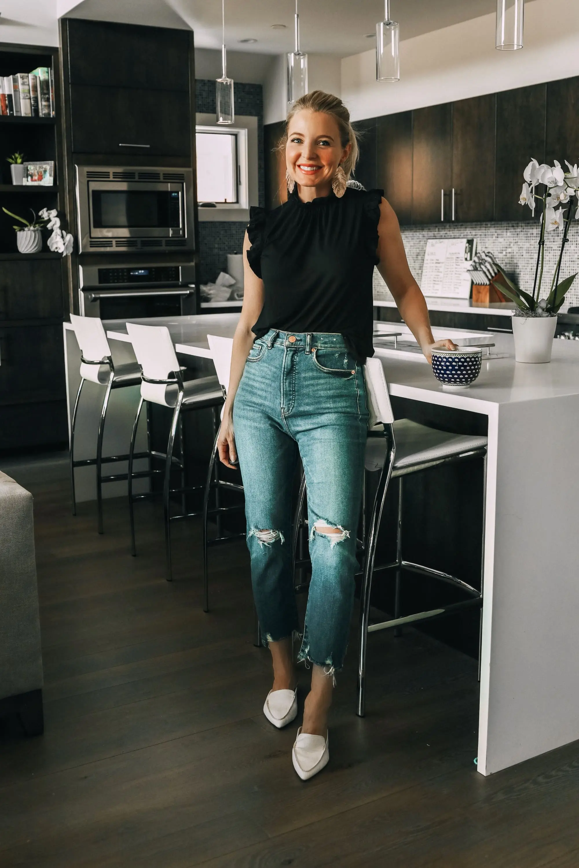 Work from home outfits that are affordable from Express featuring high rise distressed mom jeans, white loafers, black mock neck ruffle cotton top and lightweight leaf earrings