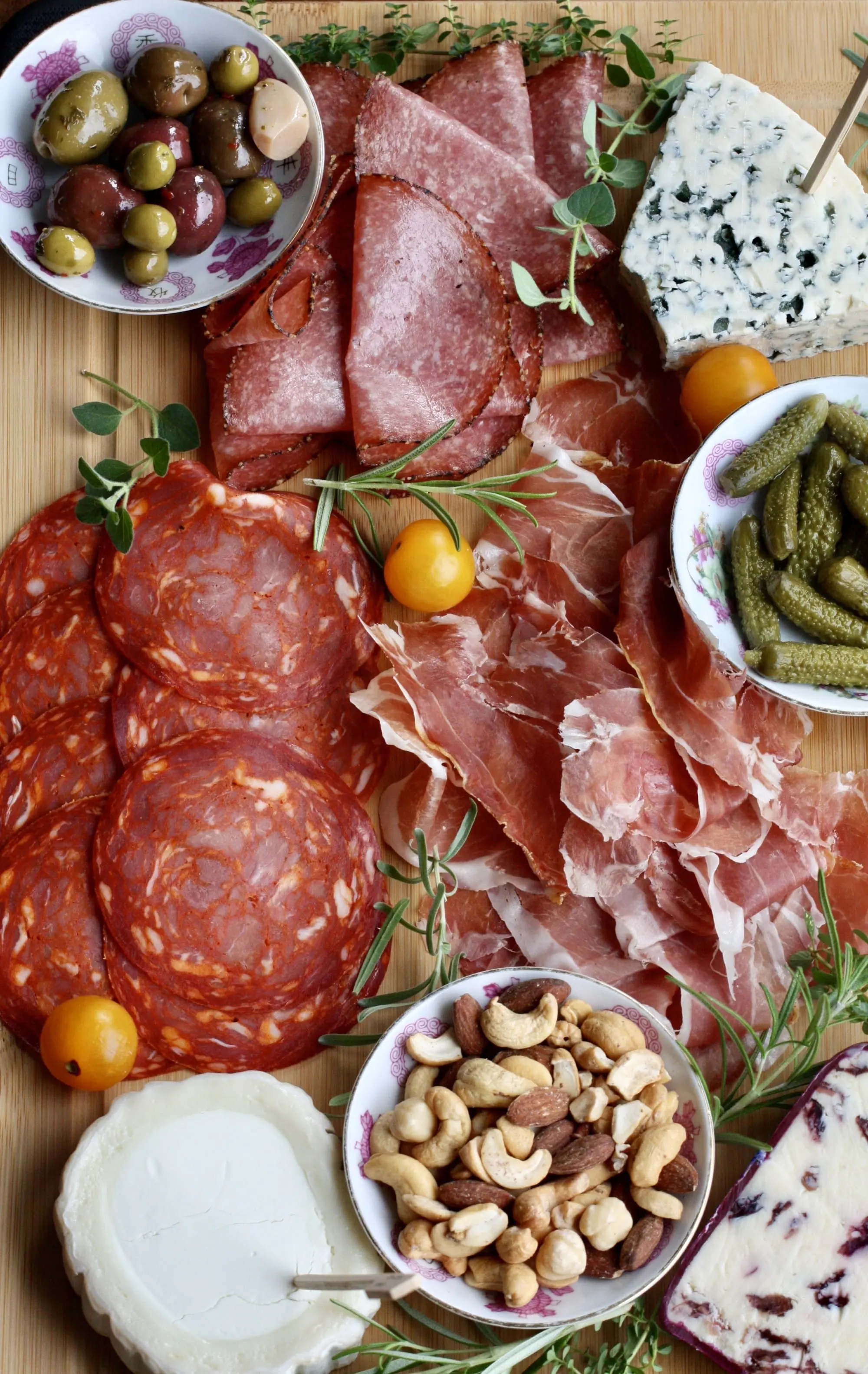 How To Make a Charcuterie Board That Will Wow Your Guests featuring a board full of cured meats, nuts and flavorful cheeses, herb garnishes, cheese board