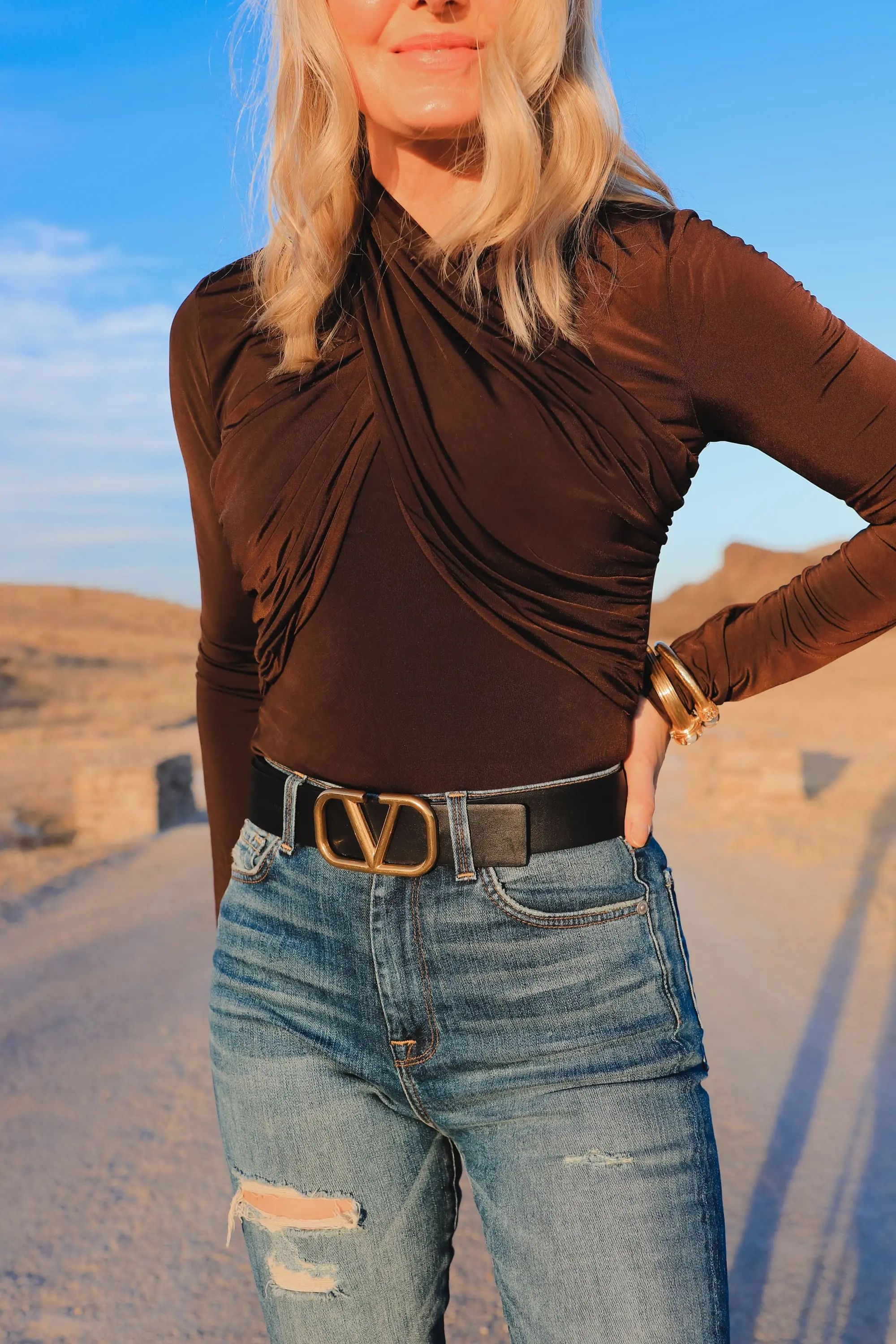 Brown and black outfit, Erin Busbee of Busbee Style wearing a dark brown wrapped neck top by Lovers + Friends tucked into 7 for all mankind ripped jeans with black snake-embossed knee-high boots and black reversible Valentino belt in west Texas