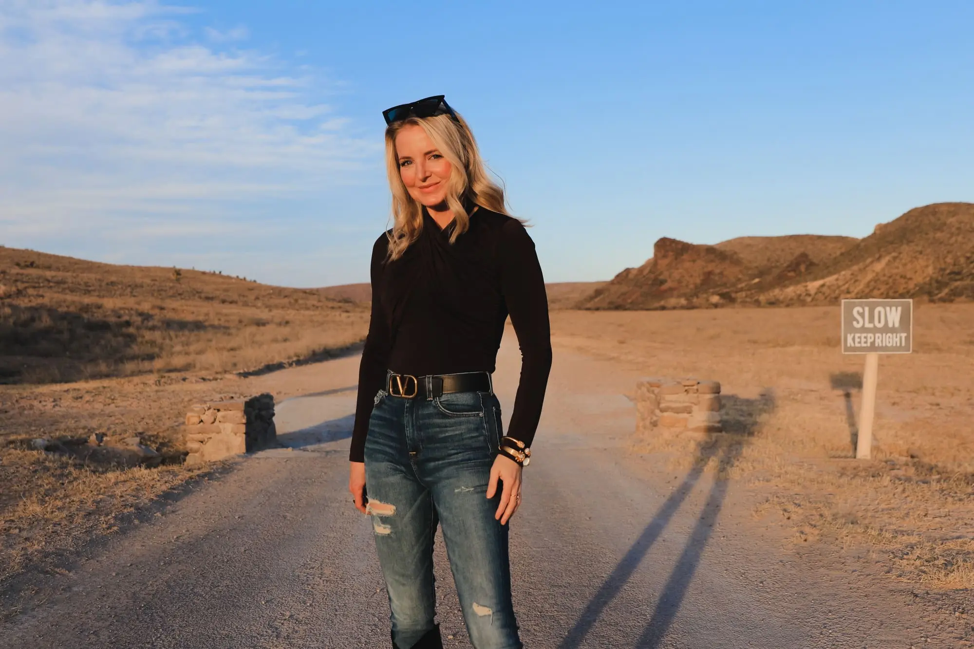 Brown and black outfit, Erin Busbee of Busbee Style wearing a dark brown wrapped neck top by Lovers + Friends tucked into 7 for all mankind ripped jeans with black snake-embossed knee-high boots and black reversible Valentino belt in west Texas