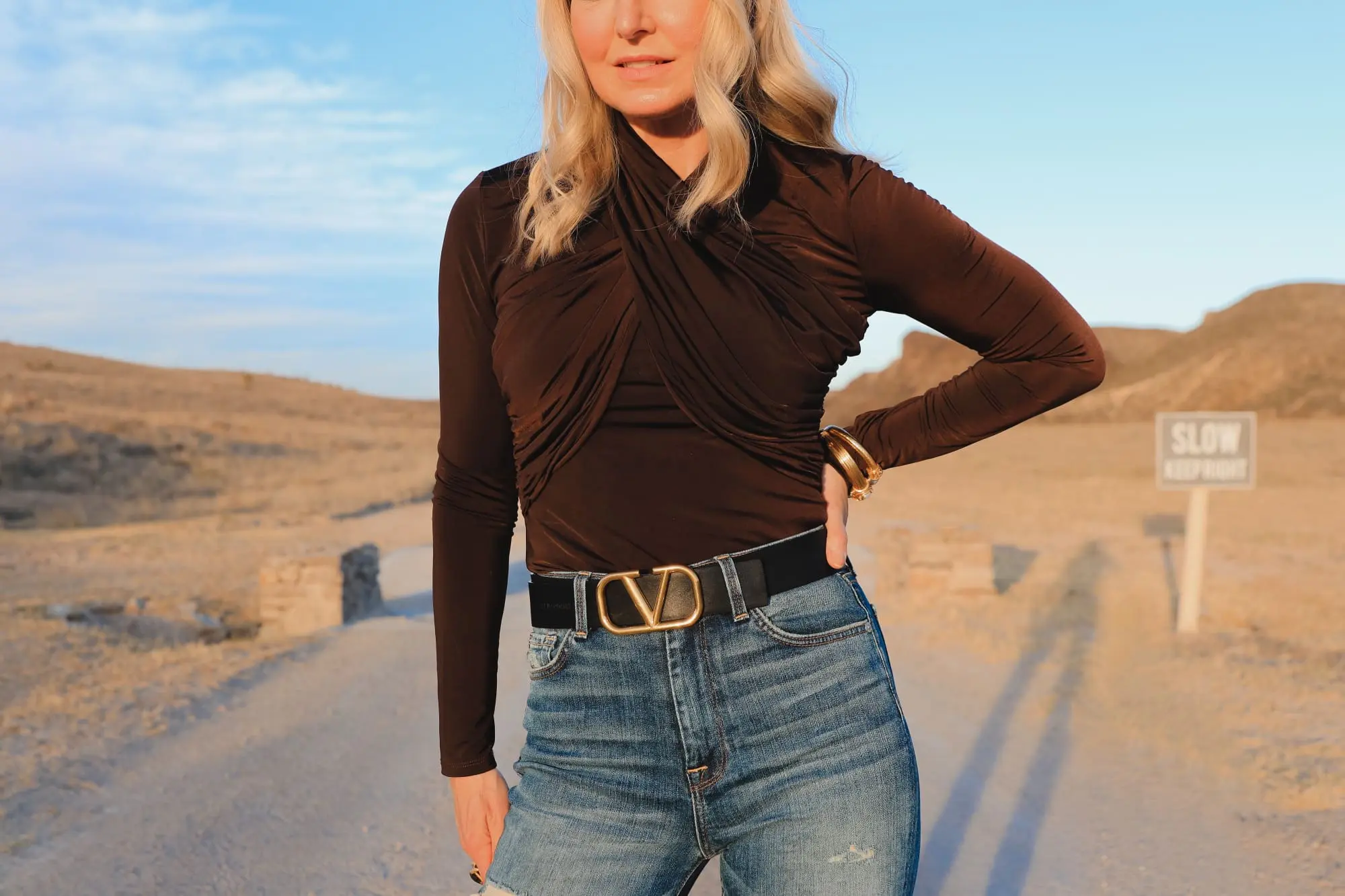 Brown and black outfit, Erin Busbee of Busbee Style wearing a dark brown wrapped neck top by Lovers + Friends tucked into 7 for all mankind ripped jeans with black snake-embossed knee-high boots and black reversible Valentino belt in west Texas