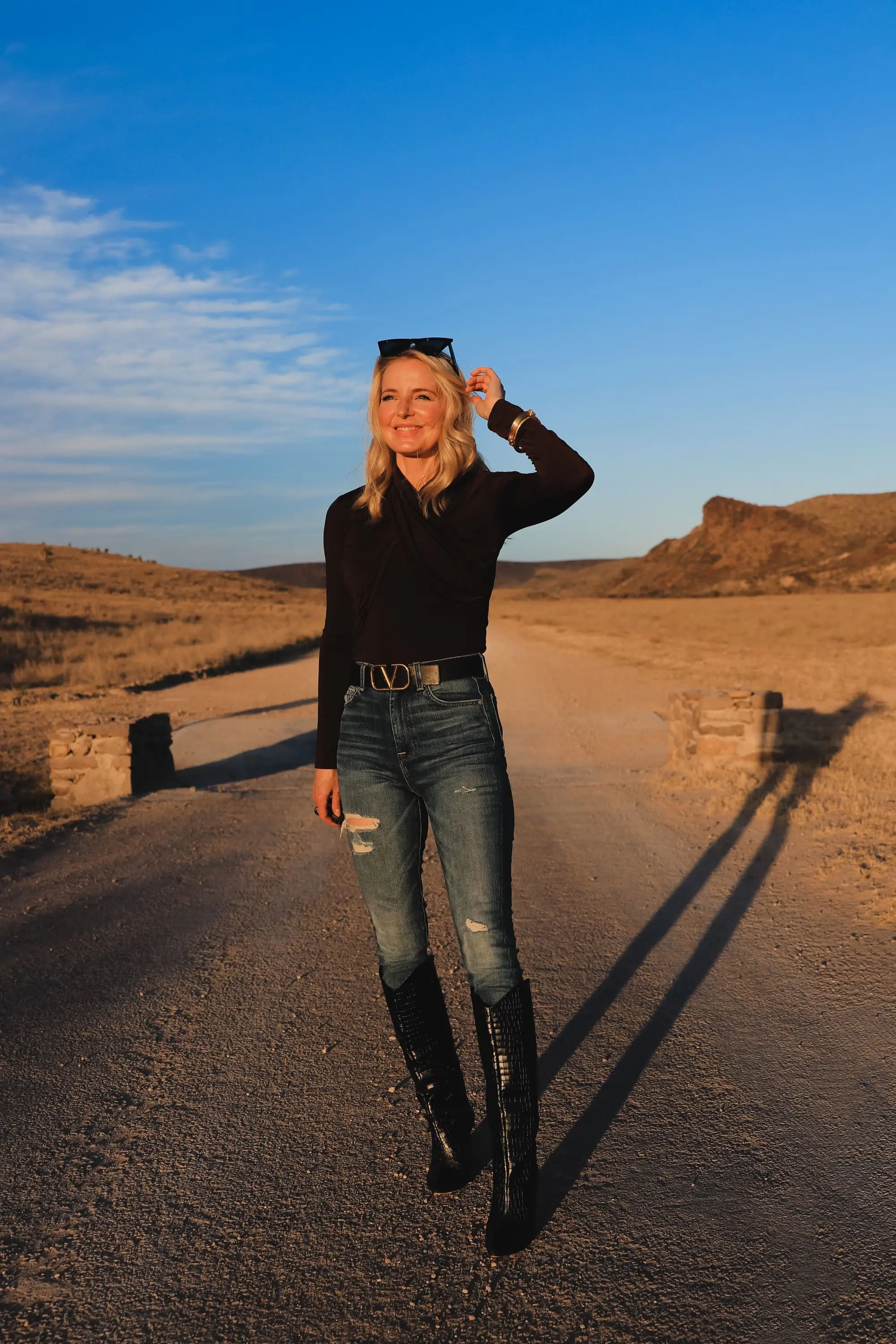 Brown and black outfit, Erin Busbee of Busbee Style wearing a dark brown wrapped neck top by Lovers + Friends tucked into 7 for all mankind ripped jeans with black snake-embossed knee-high boots and black reversible Valentino belt in west Texas