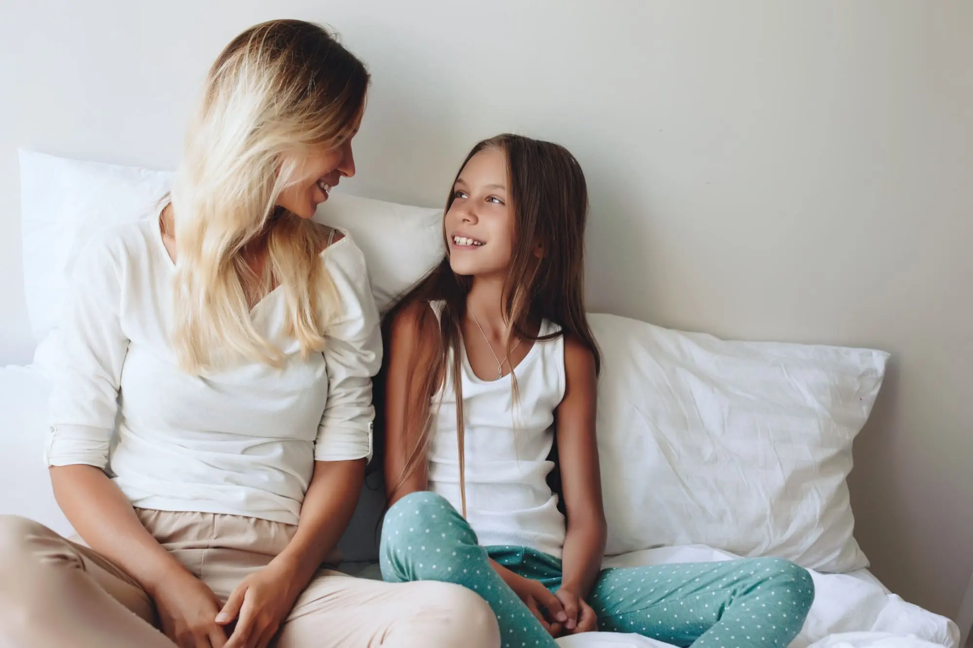 talking about sex, mother and daughter lounging in bed, smiling and talking