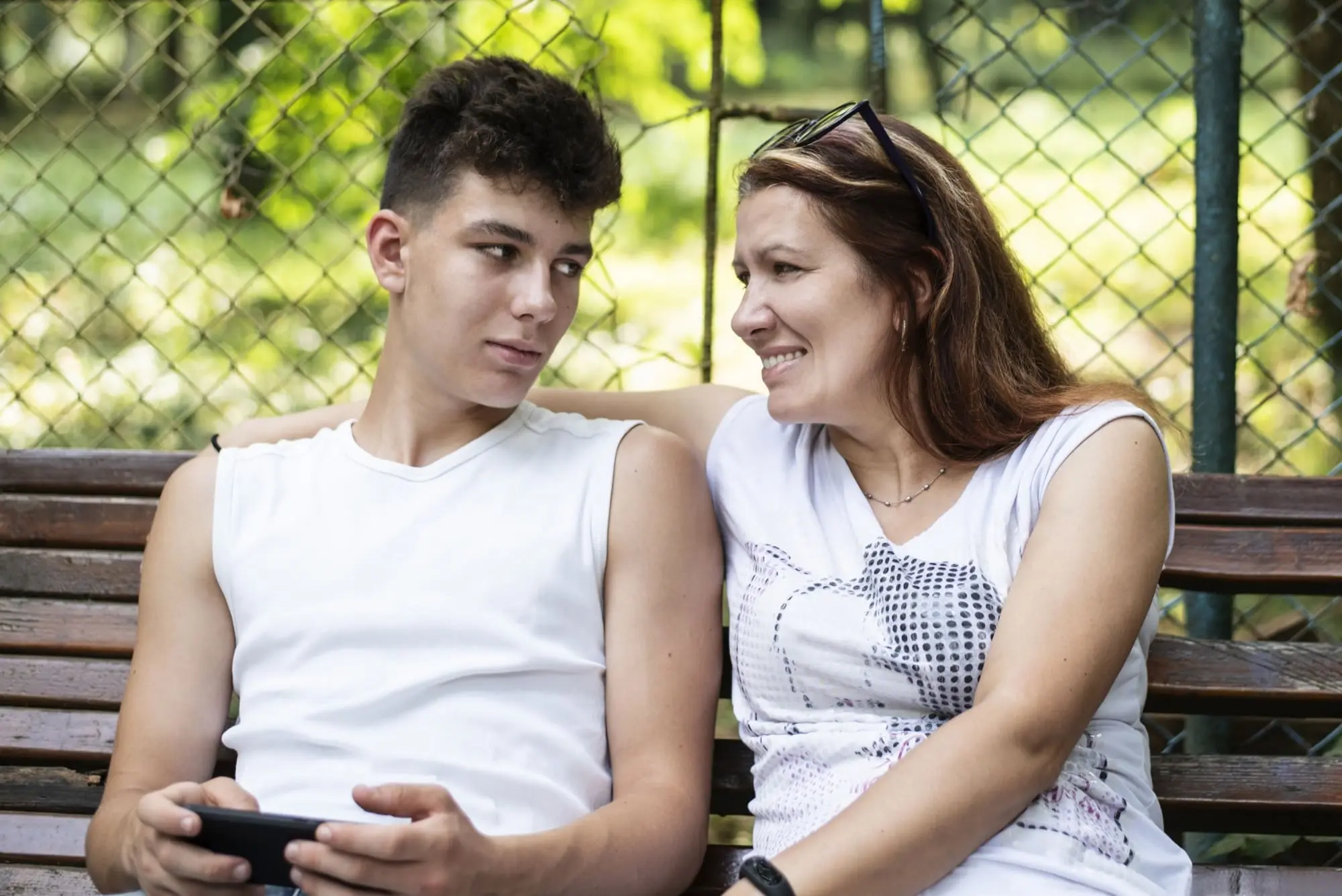 talking about sex, mother and teen son sitting on a park bench talking