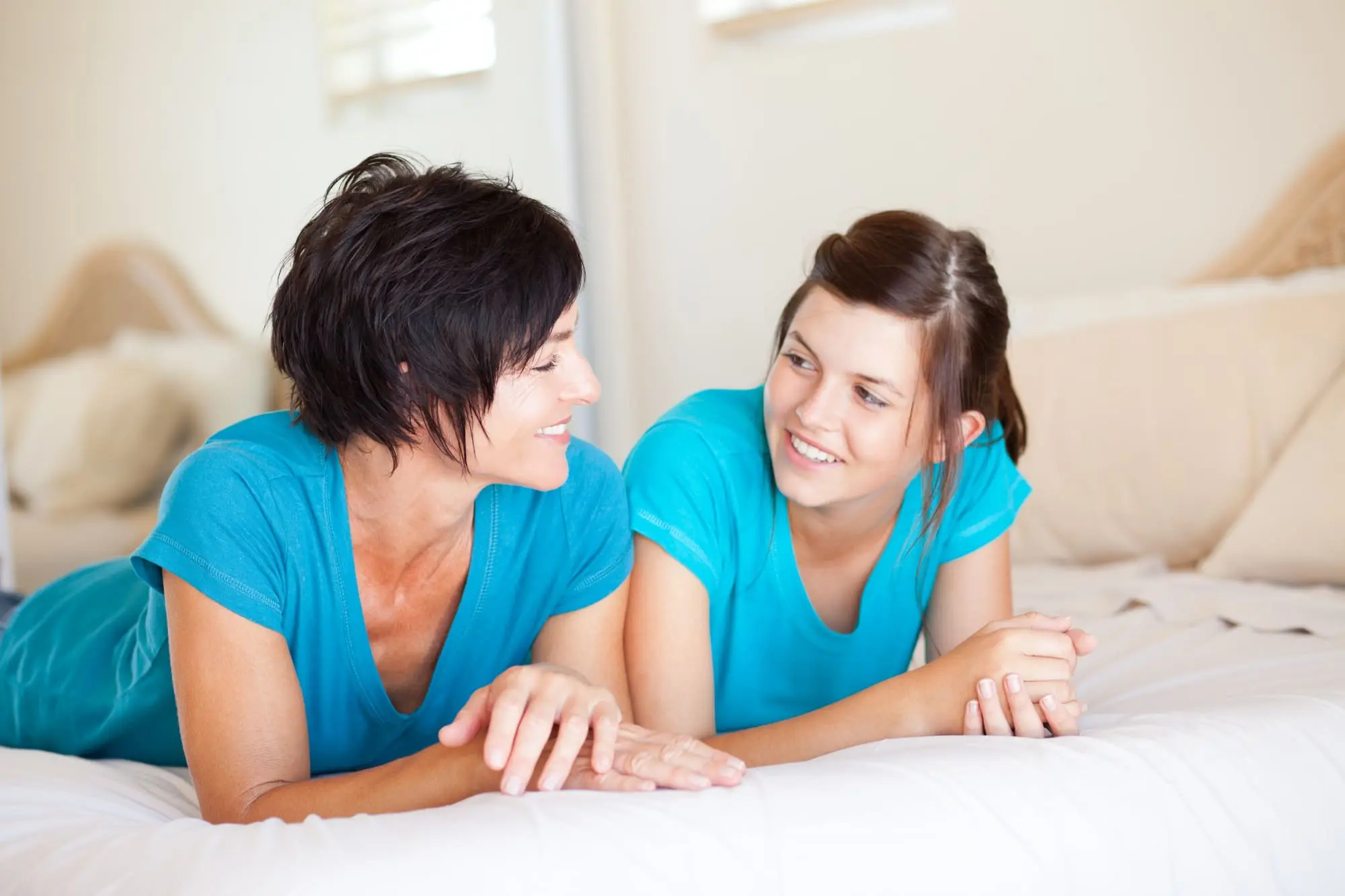 talking about sex, mother and daughter lounging in bed, smiling and talking