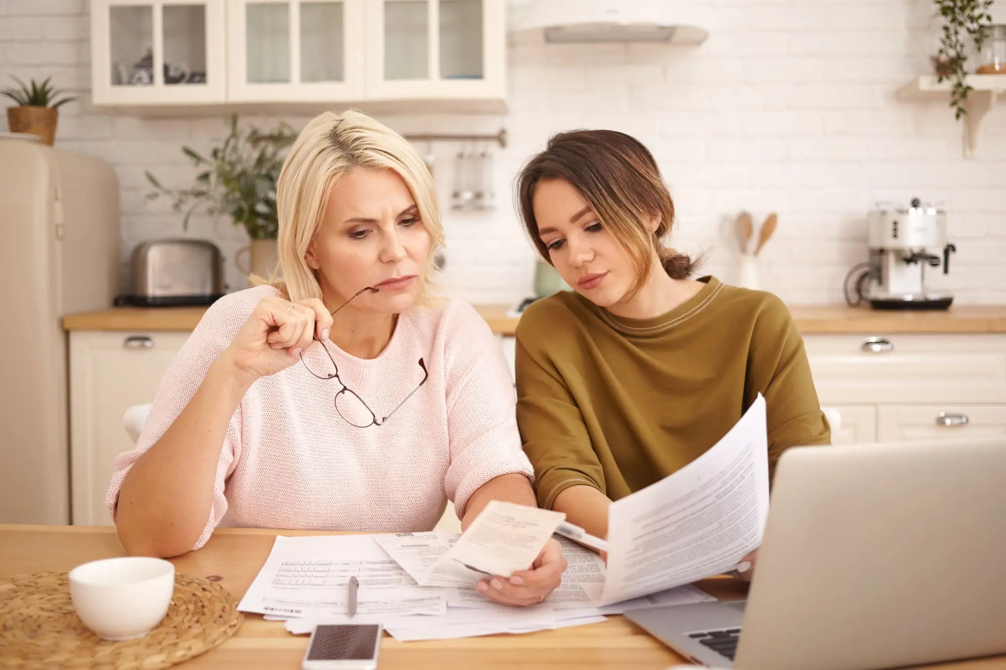 Teaching kids about money, mom and teen girl review expenses together at the kitchen table