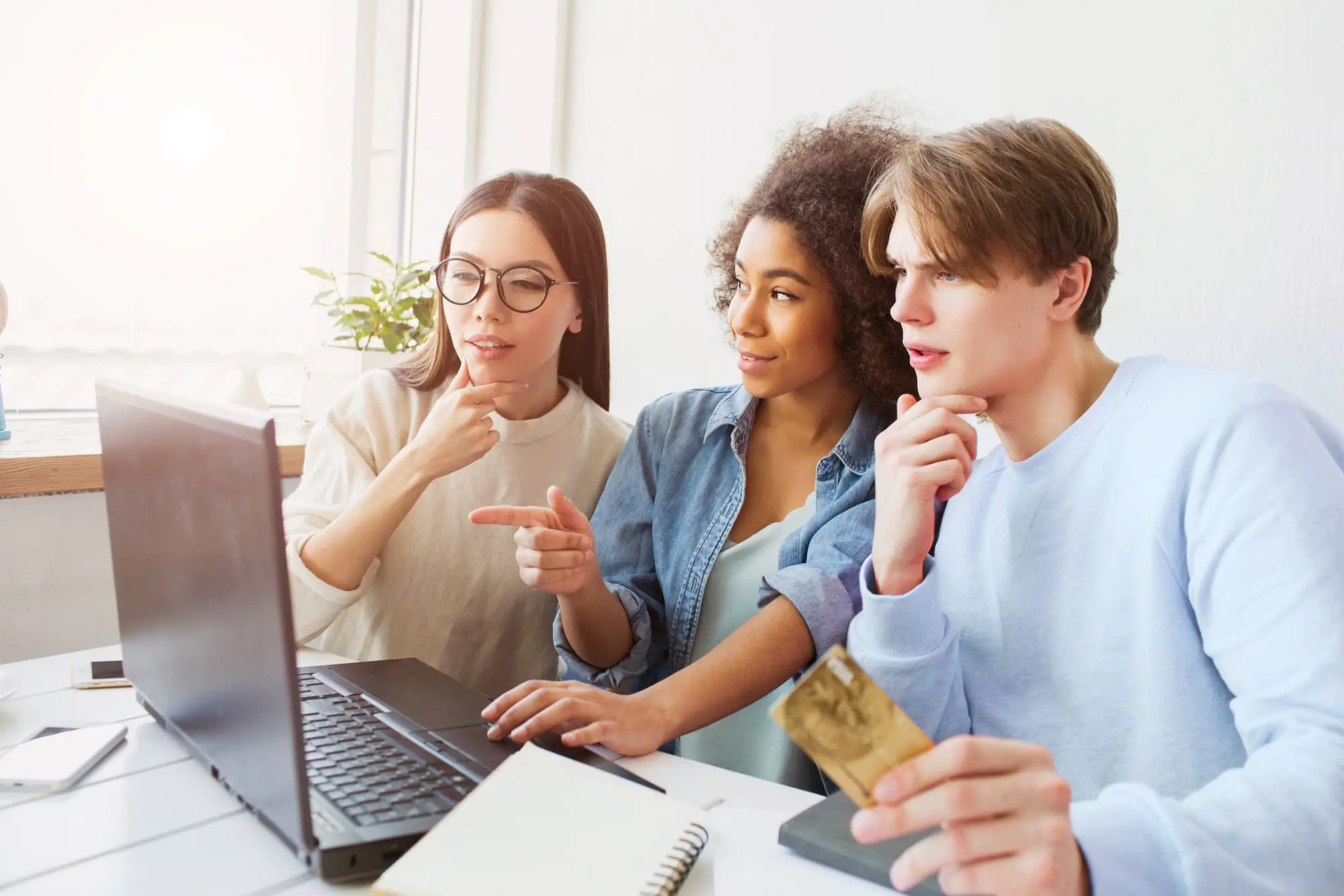 Teaching kids about money, three teens discussing finances in front of a laptop