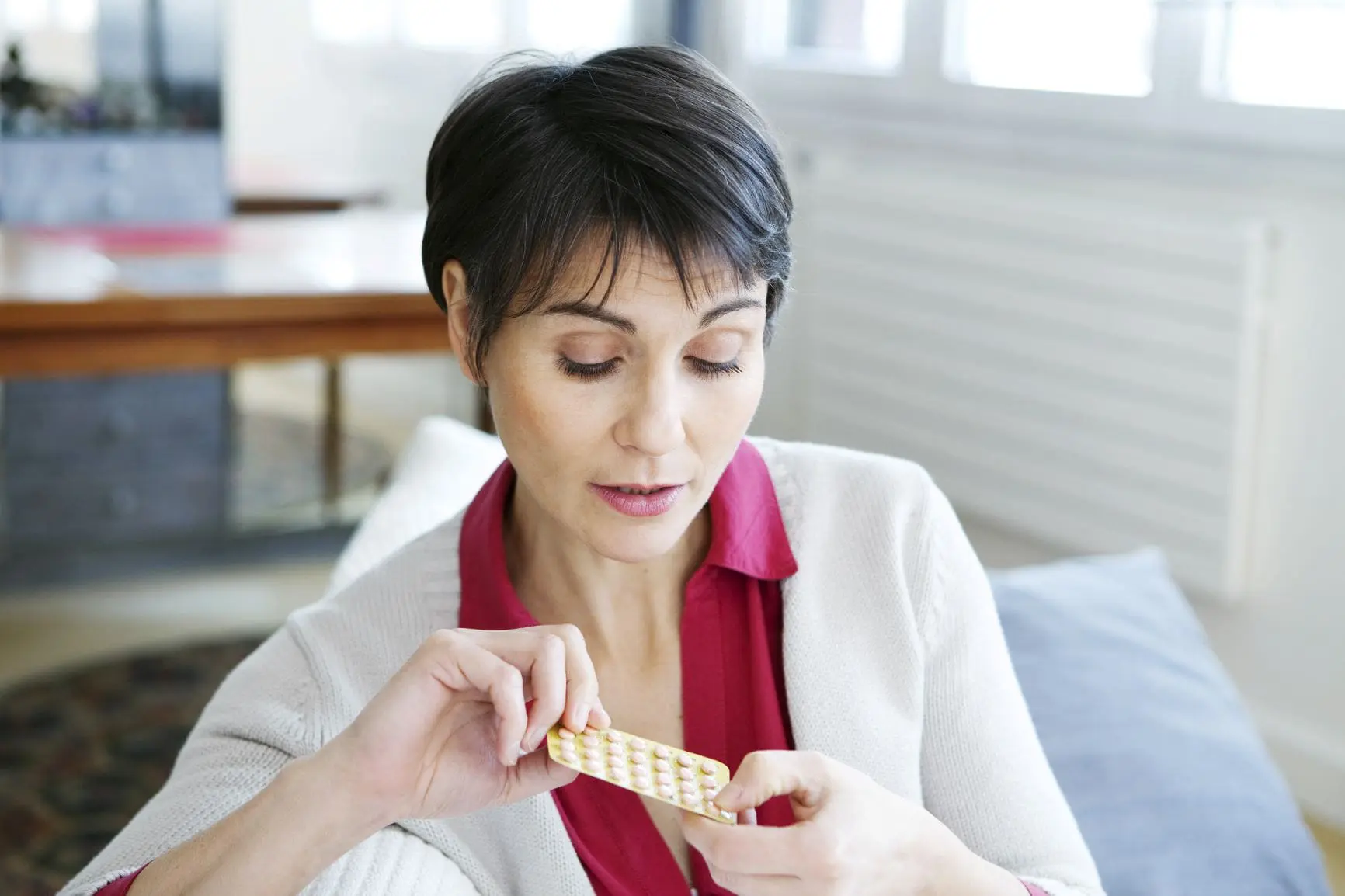 better sex after menopause, Dark short-haired woman in red blouse and white sweater taking hormones