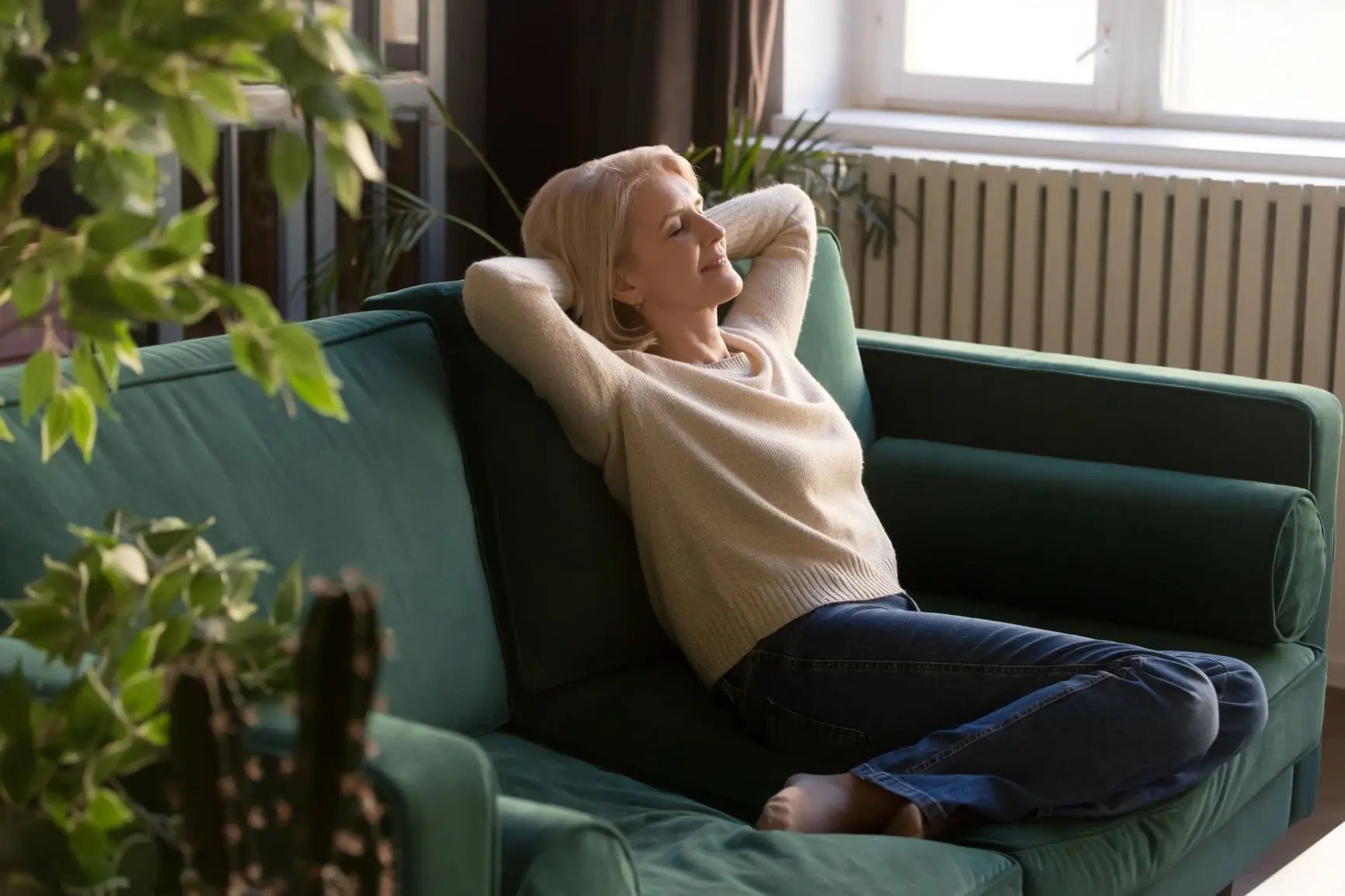 Petite Blond in pink sweater and jeans dreaming on jade couch with plants, manifest your dream life, manifestation for beginners