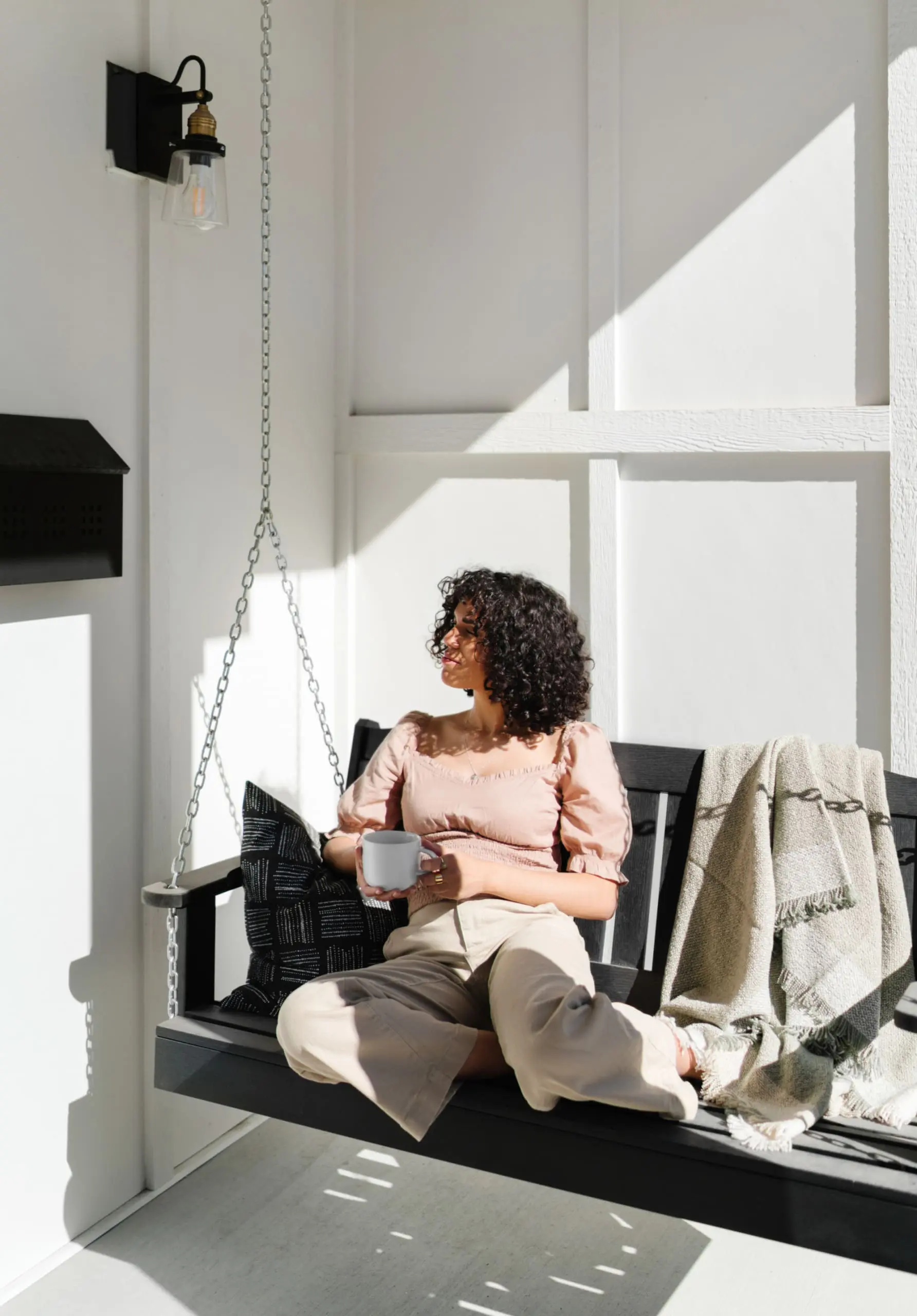 Self-care Guide, self-care habits, self-care in the new year. wellness in the new year, Dark-haired woman drinking hot beverage on porch swing