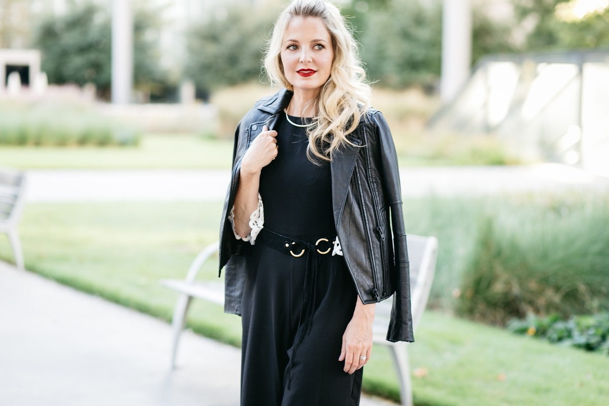 Erin Busbee wearing a black moto jacket by joie over a black wide leg jumpsuit by Asos with a gold and black belt and a kendra scott gold choker necklace