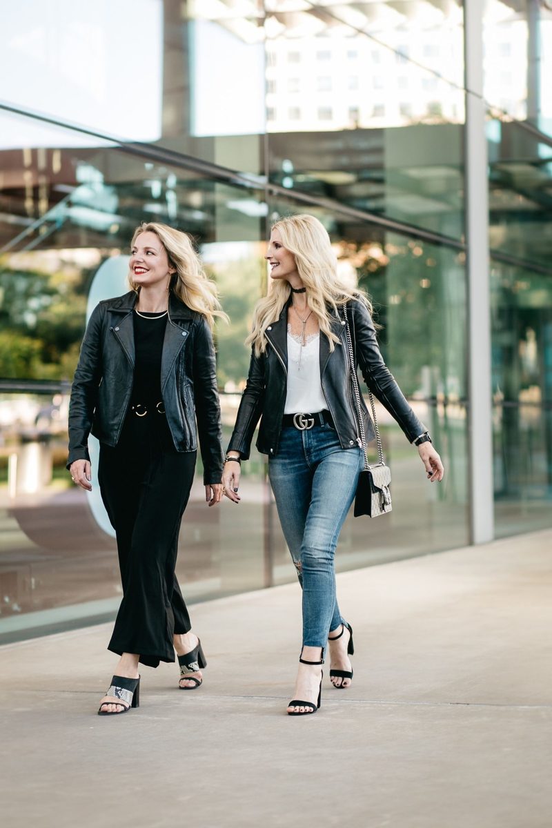 two fashion bloggers, erin busbee and heather anderson wearing black moto jackets in two different ways, one over a black jumpsuit, the other over a tee and jeans.