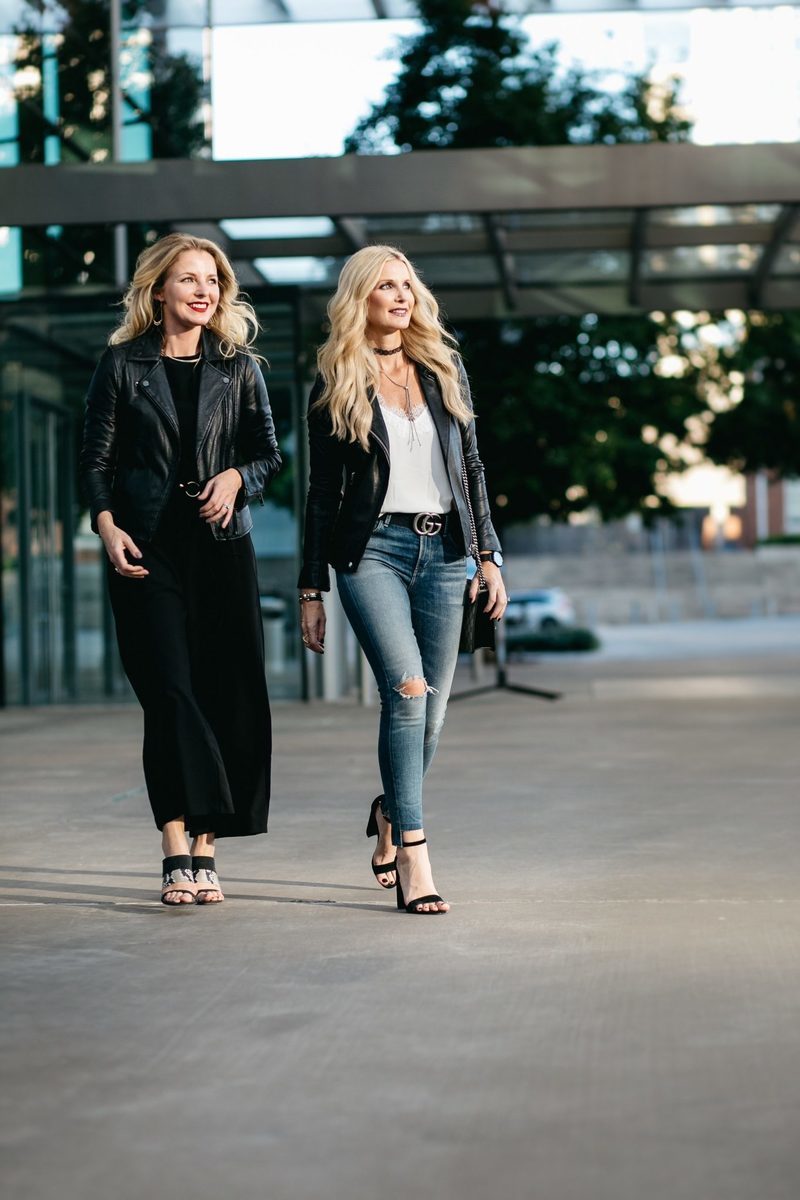 two fashion bloggers, erin busbee and heather anderson wearing black moto jackets in two different ways, one over a black jumpsuit, the other over a tee and jeans.