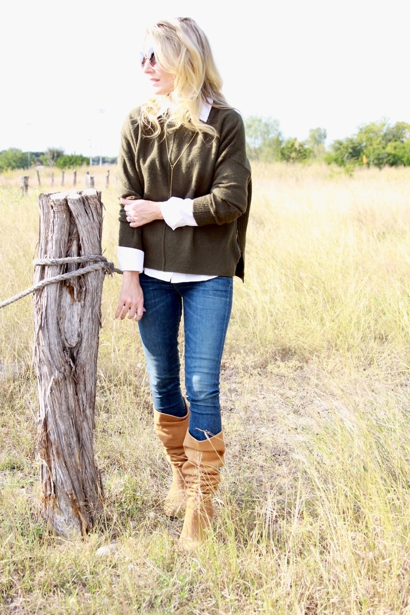 standing in the field in a cozy green sweater, white button down shirt, dark wash jeans and beautiful light brown boots by sam edelman
