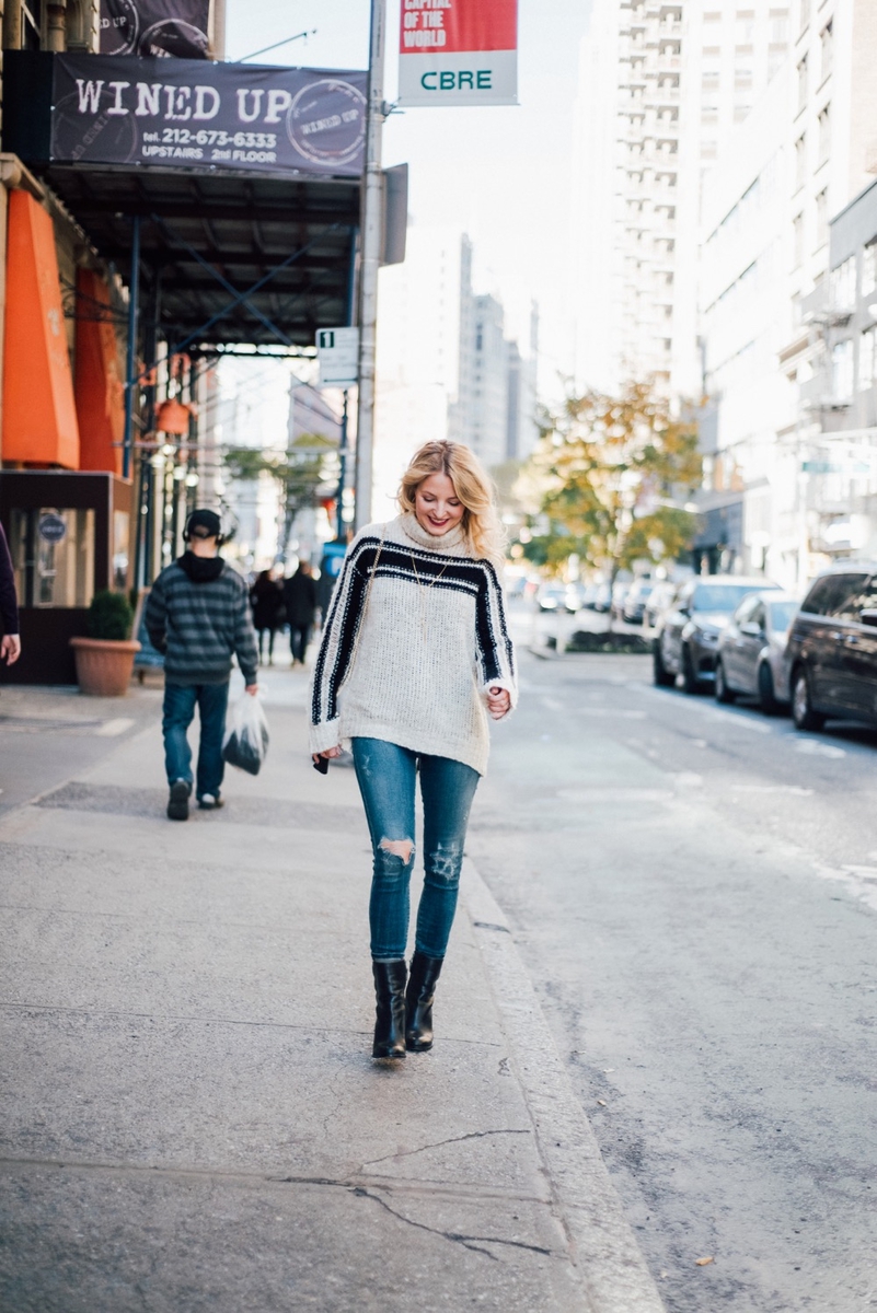 erin busbee walking down new york city street wearing casual outfit including dark wash citizens of humanity rocket slightly distressed skinny jeans, mid-calf black booties by sam edelman, and a pam and gela racing stripe turtleneck sweater