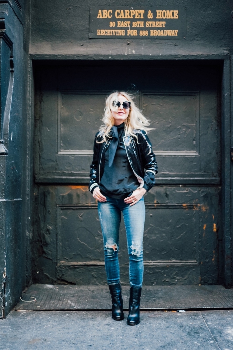 erin busbee in new york city wearing a tie neck black blouse a sequin bomber jacket, skinny, distressed jeans by citizens of humanity with sam edelman mid-calf booties