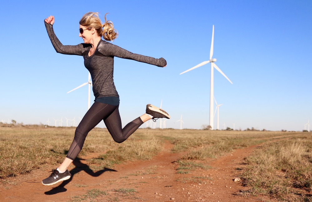 running in the air wearing zella exercise top and pants and under armour running sneakers