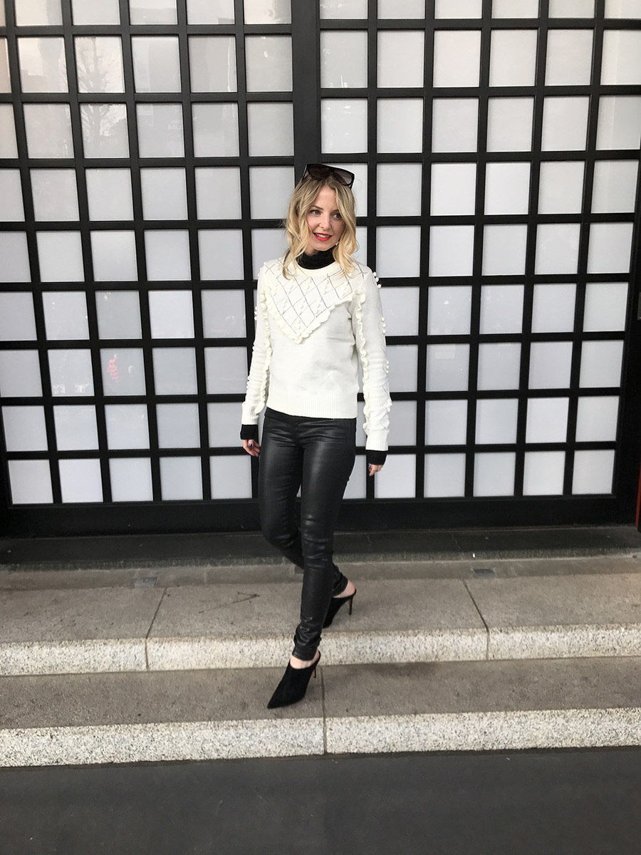 Erin busbee wearing a white topshop sweater with pom pom detailing, faux leather black skinny jeans by citizens of humanity called the "rocket" jeans, mules by marc fisher in black suede and flat top sunglasses that look like Givenchy but only cost $10 from Amazon fashion