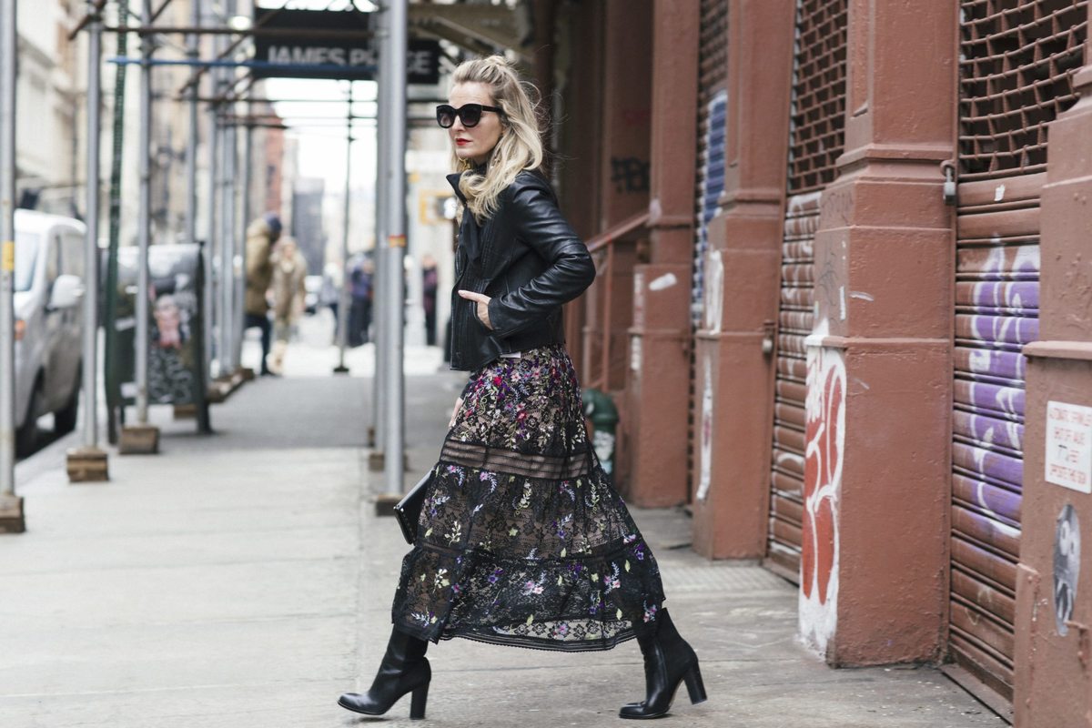 Erin Busbee in NYC for New York Fashion Week 2017 wearing nicole miller blooming floral print dress in black with black leather moto jacket by Joie, topknot in hair, black mid-calf-sam edelman boots and black sunglasses