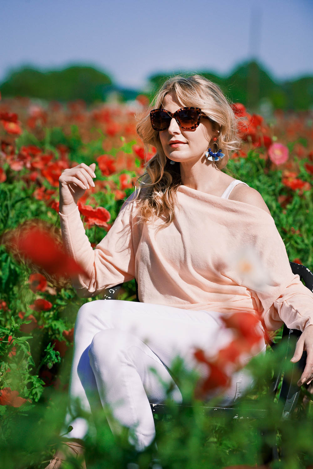 How to wear pastel colors, featuring an off-shoulder lightweight free people sweater with white AG jeans and baublebar pom pom earrings, sitting in wildseed farms in fredericksburg texas in a poppy field on erin busbee, fashion blogger and youtuber