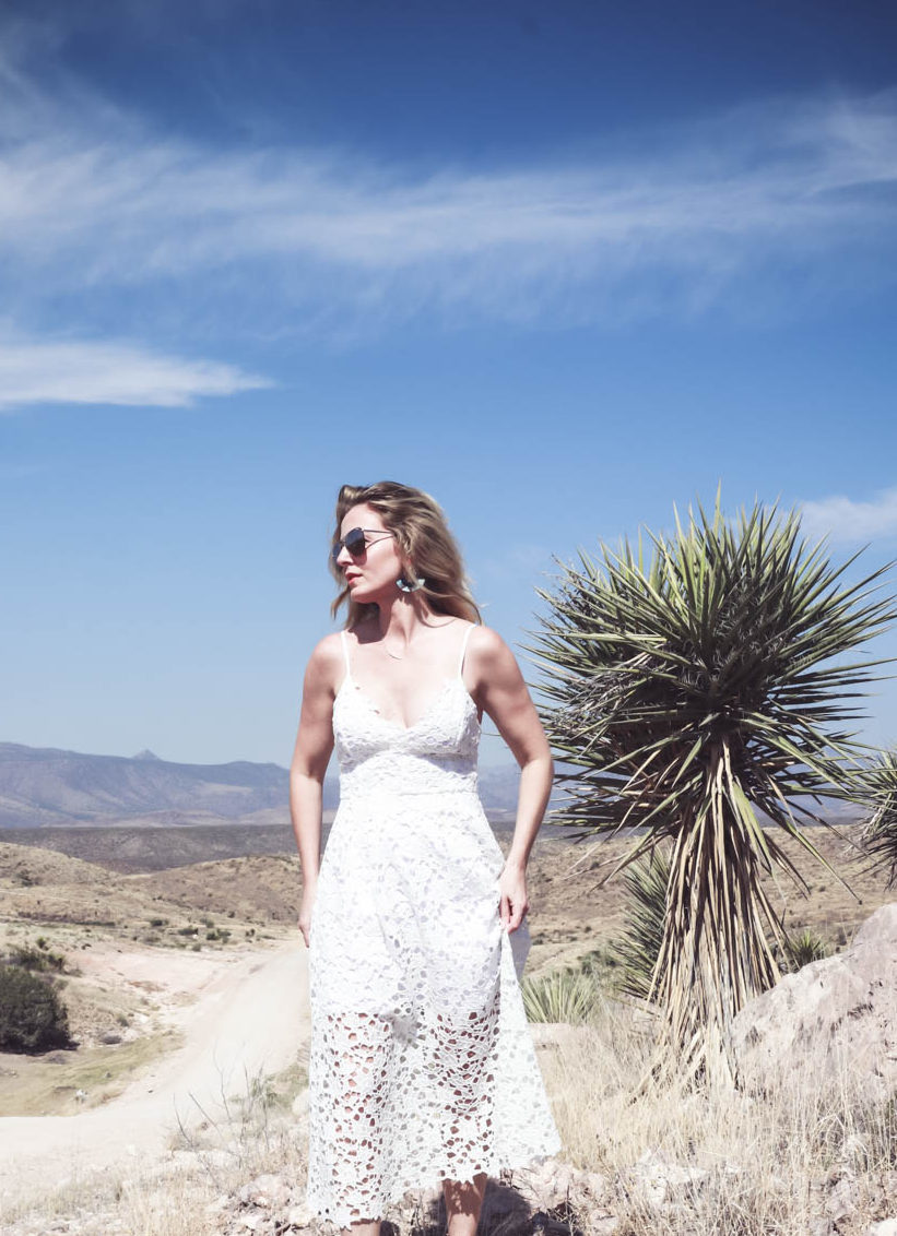 Fashion blogger and fashion youtuber, erin busbee of busbeestyle.com, posing by a dagger cactus, wearing a white lace dress by ASTR, nude leather espadrille sandals by Marc Fisher (super comfortable) and the mirrored aviator sunglasses are by Quay Australia in Marfa Texas at Cibolo Creek Ranch