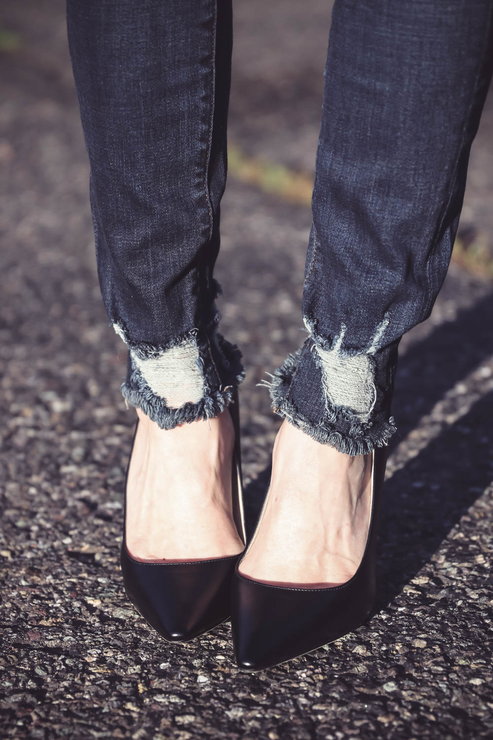 Denim Trends, Good American distressed jeans, high rise, distressed at ankle with black sleeveless sweater, and jimmy choo pumps