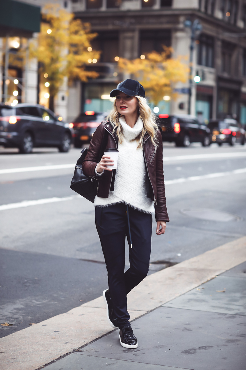 Gym to street pants, perfect for creating the athleisure look on fashion blogger over 40, Erin Busbee of Busbee Style paired with fuzzy white turtleneck sweater, doma leather hooded leather jacket and Henri Bendel leather jetsetter backpack with patent leather sneakers by Kenneth Cole