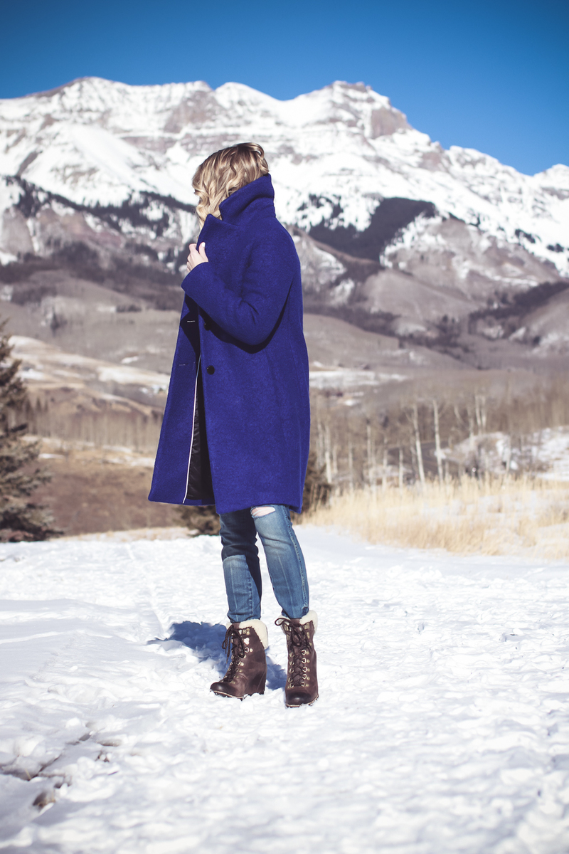blue coat by Elie Tahari, boiled wool winter coat in beautiful color on fashion blogger over 40, Erin Busbee of Busbee Style wearing Henri Bendel sunglasses, Sorel conquest wedge booties, Amo twist skinny jeans and a Bloomingdales fuzzy white sweater in mountain village, colorado, snowy mountains