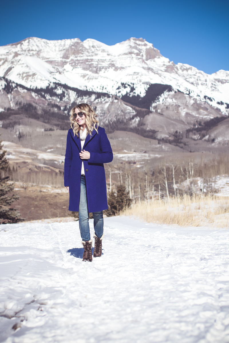 blue coat by Elie Tahari, boiled wool winter coat in beautiful color on fashion blogger over 40, Erin Busbee of Busbee Style wearing Henri Bendel sunglasses, Sorel conquest wedge booties, Amo twist skinny jeans and a Bloomingdales fuzzy white sweater in mountain village, colorado, snowy mountains