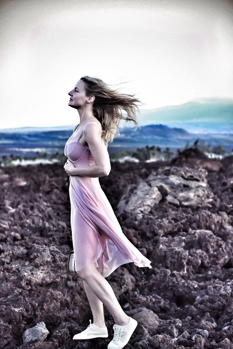 blond woman standing on lava rock in Hawaii wearing a blush corset sheer swim dress by Norma Kamali and floral headband from Nordstrom