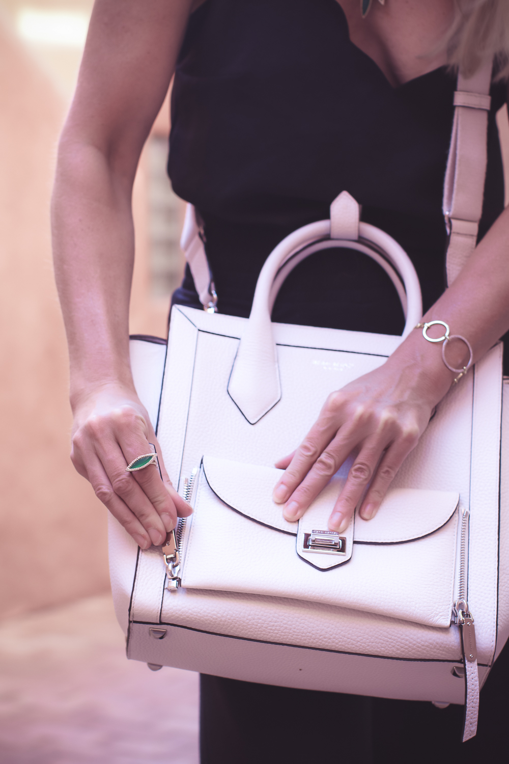 chic and sophisticated backpacks for grown ups by Henri Bendel, featuring blonde woman carrying a white Rivington convertible tote and backpack wearing all black with dainty gold and green jewelry