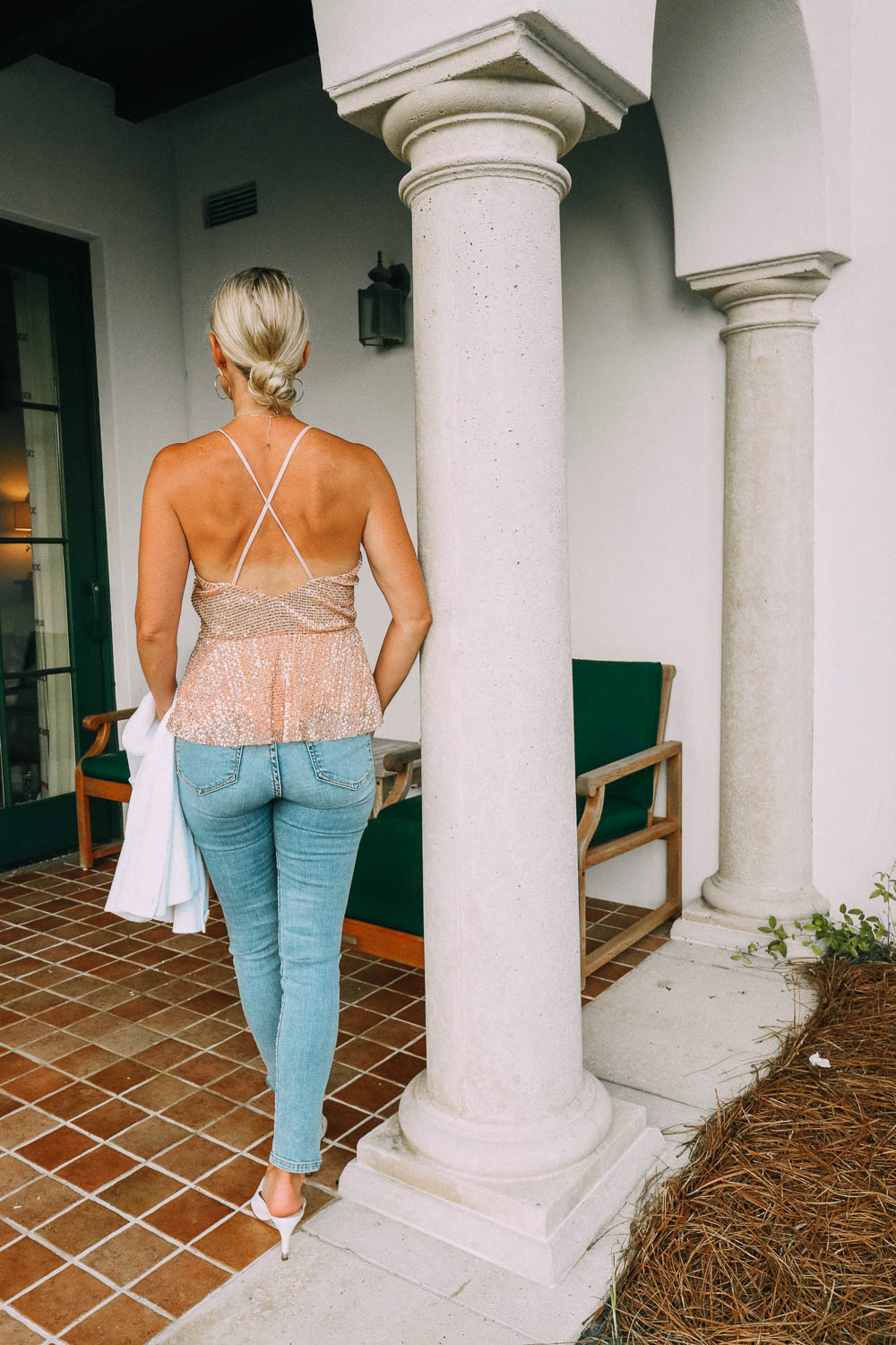 blonde woman in Sea Island, Georgia wearing Good American split hem jeans, affordable sparkle top with criss cross back, white blazer, and white mules