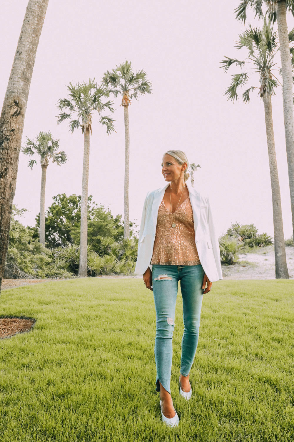 blonde woman in Sea Island, Georgia wearing Good American split hem jeans, affordable sparkle top, white blazer, and white mules