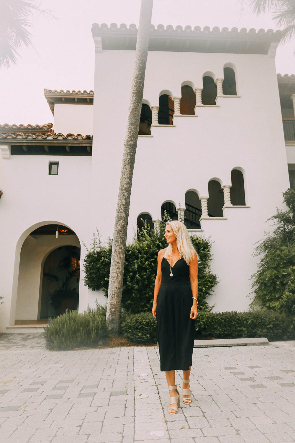 blonde woman in Sea Island, Georgia wearing a black lace up jumpsuit and sandals 