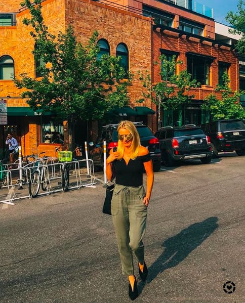 woman walking in green jogger pants and a black express off the shoulder top, carrying henri bendel hobo bag in Aspen, colorado