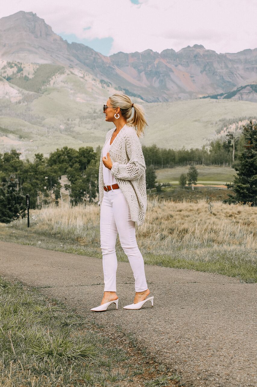 blonde woman with hair in pony tail in Telluride, Colorado wearing a Free People cardigan, white skinny jeans, Louise et Cie white mules, and Madewell tee