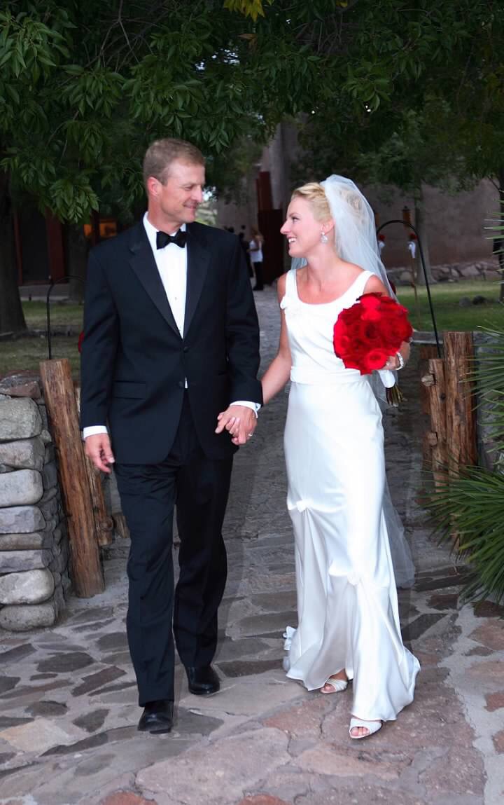 Fashion Blogger Erin Busbee of Busbee Style in wedding gown carrying red bouquet with husband