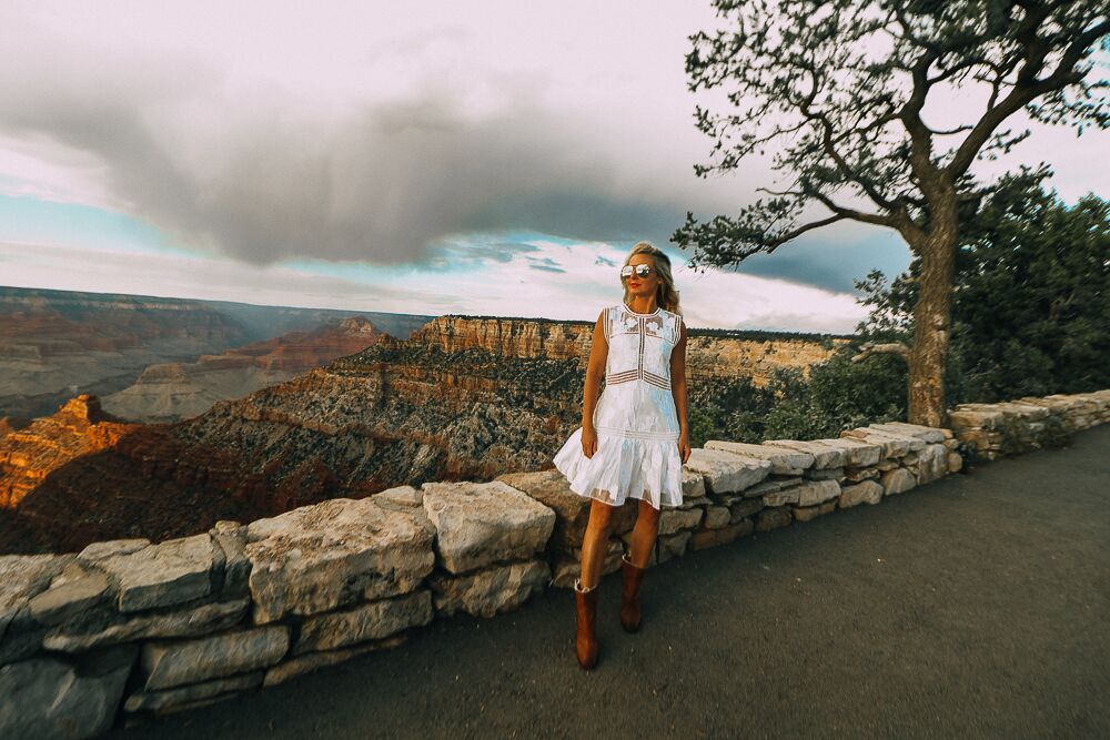 blonde woman wearing a white lace dress with brown booties visiting the grand canyon