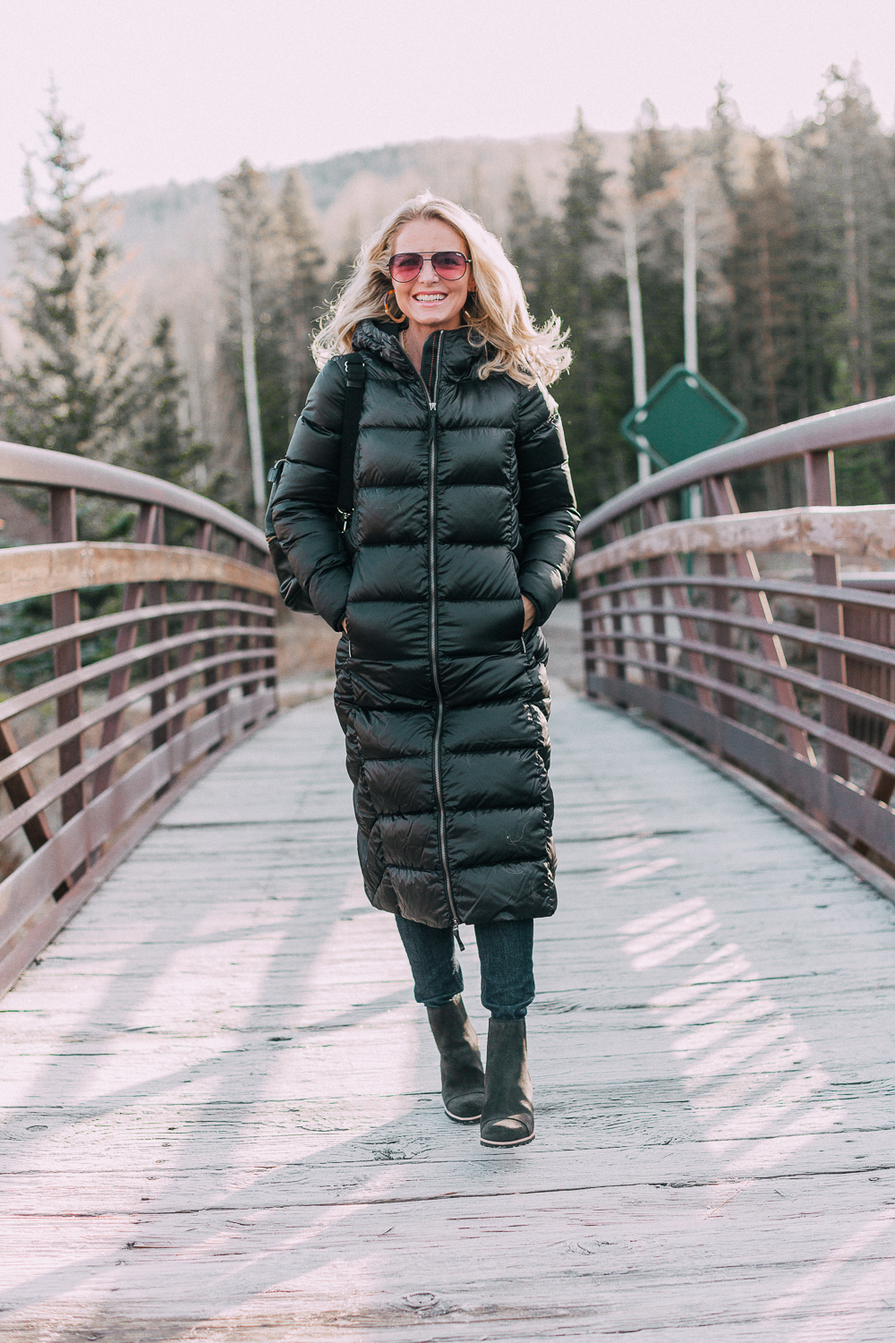 best puffer coats for women by Parajumpers from Bloomingdales in black, long puffer coat paired with dark jeans, black Ugg wedge booties on blonde woman