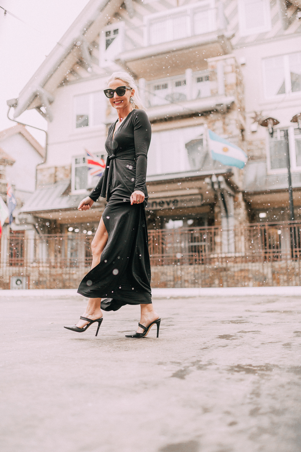Unexpected holiday party outfits featuring a long black maxi dress with high slit to show off legs and a knot under the bust on blonde fashion blogger in telluride, colorado in the snow