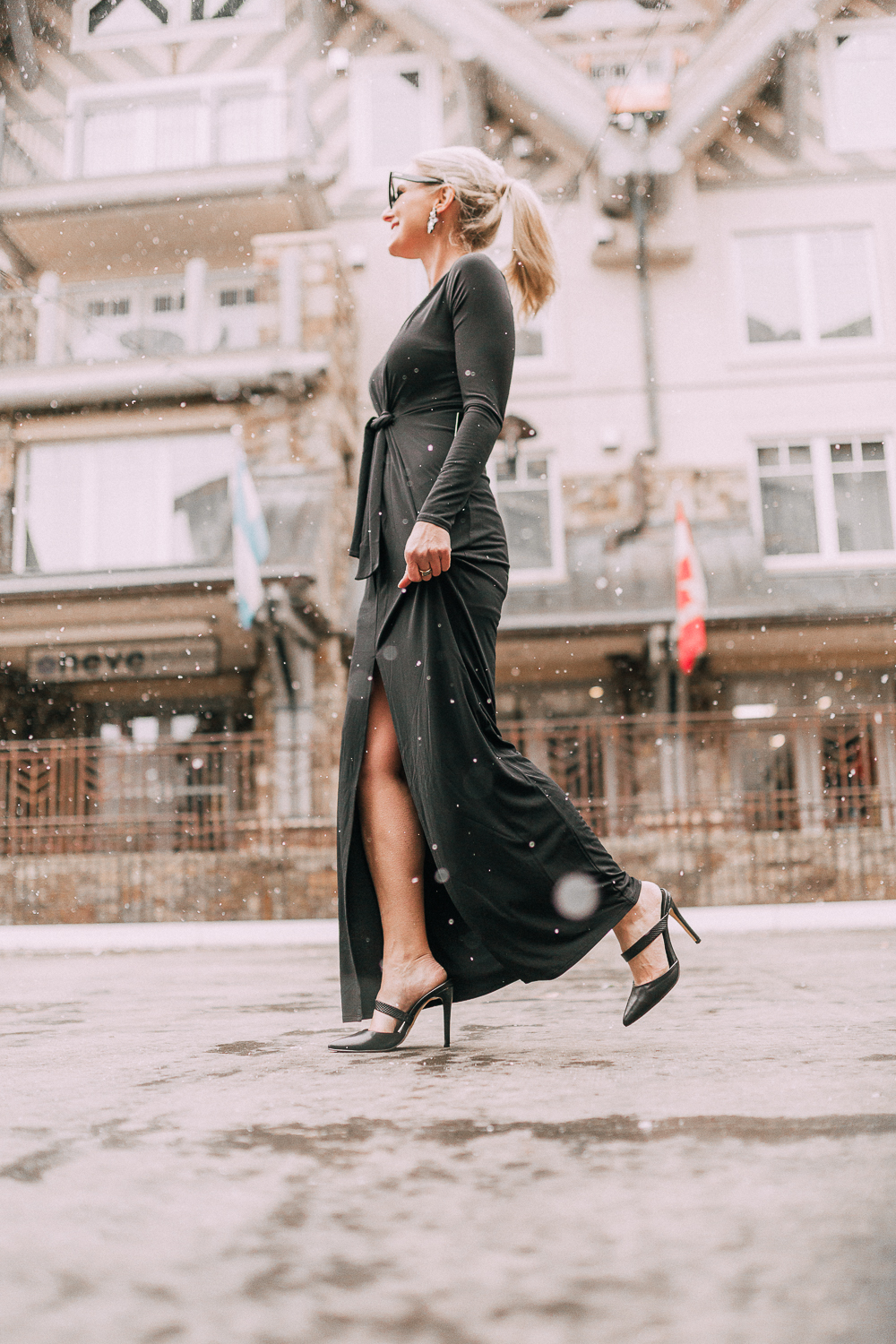 Unexpected holiday party outfits featuring a long black maxi dress with high slit to show off legs and a knot under the bust on blonde fashion blogger in telluride, colorado in the snow