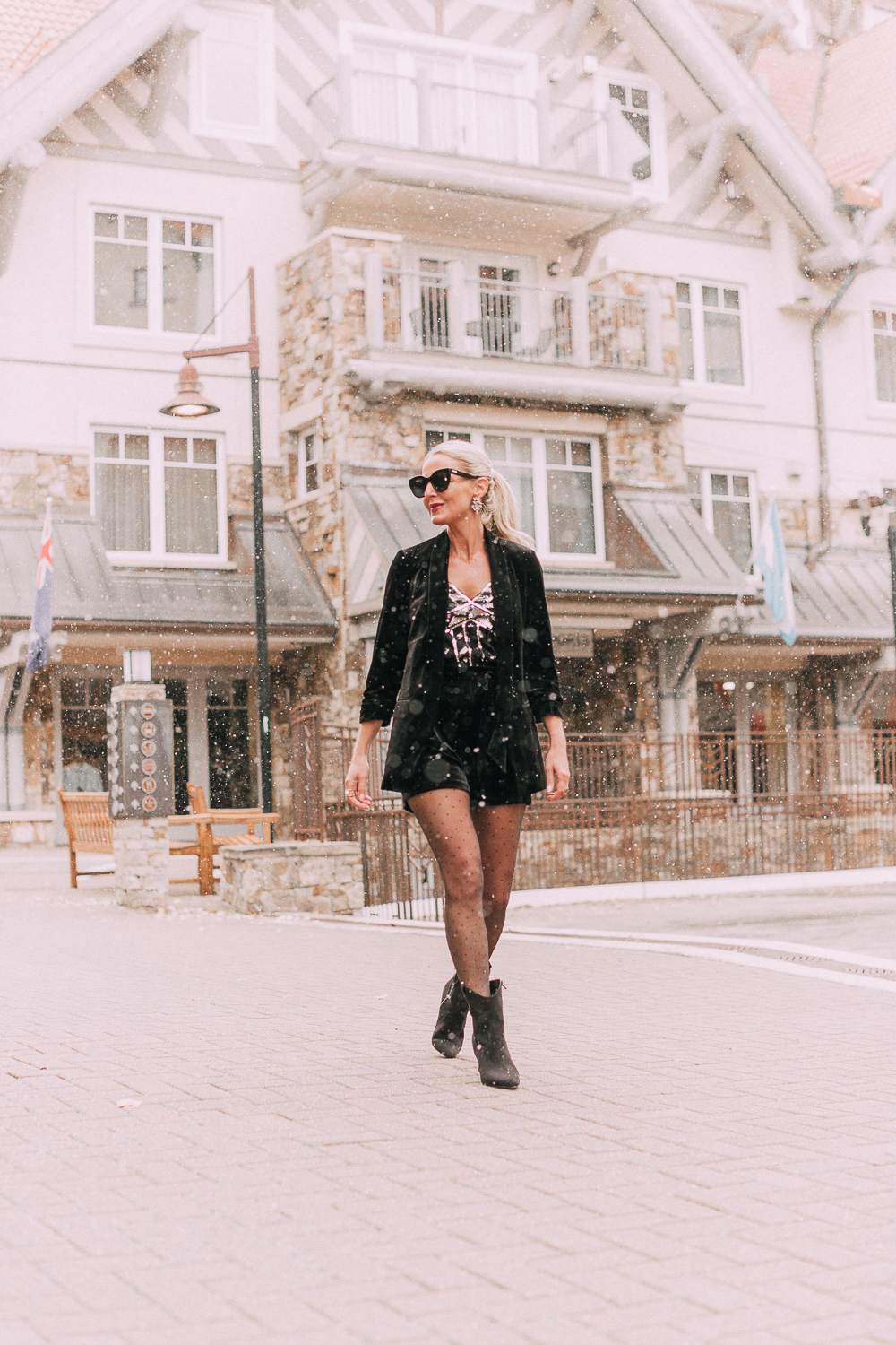 Unexpected holiday party outfits featuring a velvet Shorts suit from Express paired with Western black booties, and polka dot black tights on fashion blogger with blonde hair
