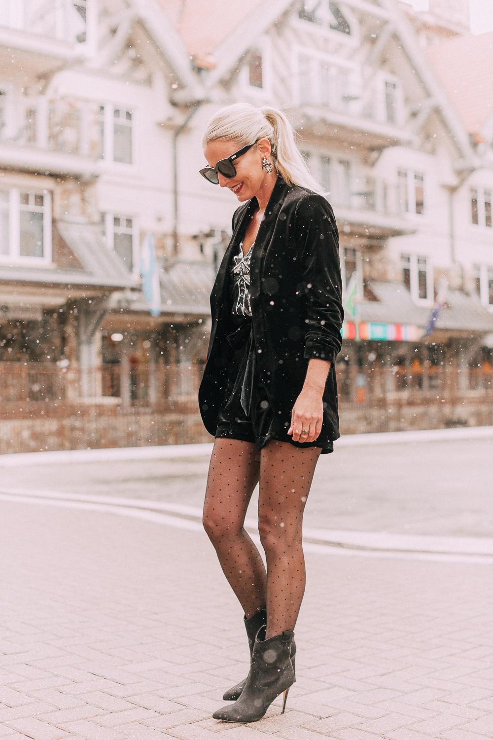 Unexpected holiday party outfits featuring a velvet Shorts suit from Express paired with Western black booties, and polka dot black tights on fashion blogger with blonde hair