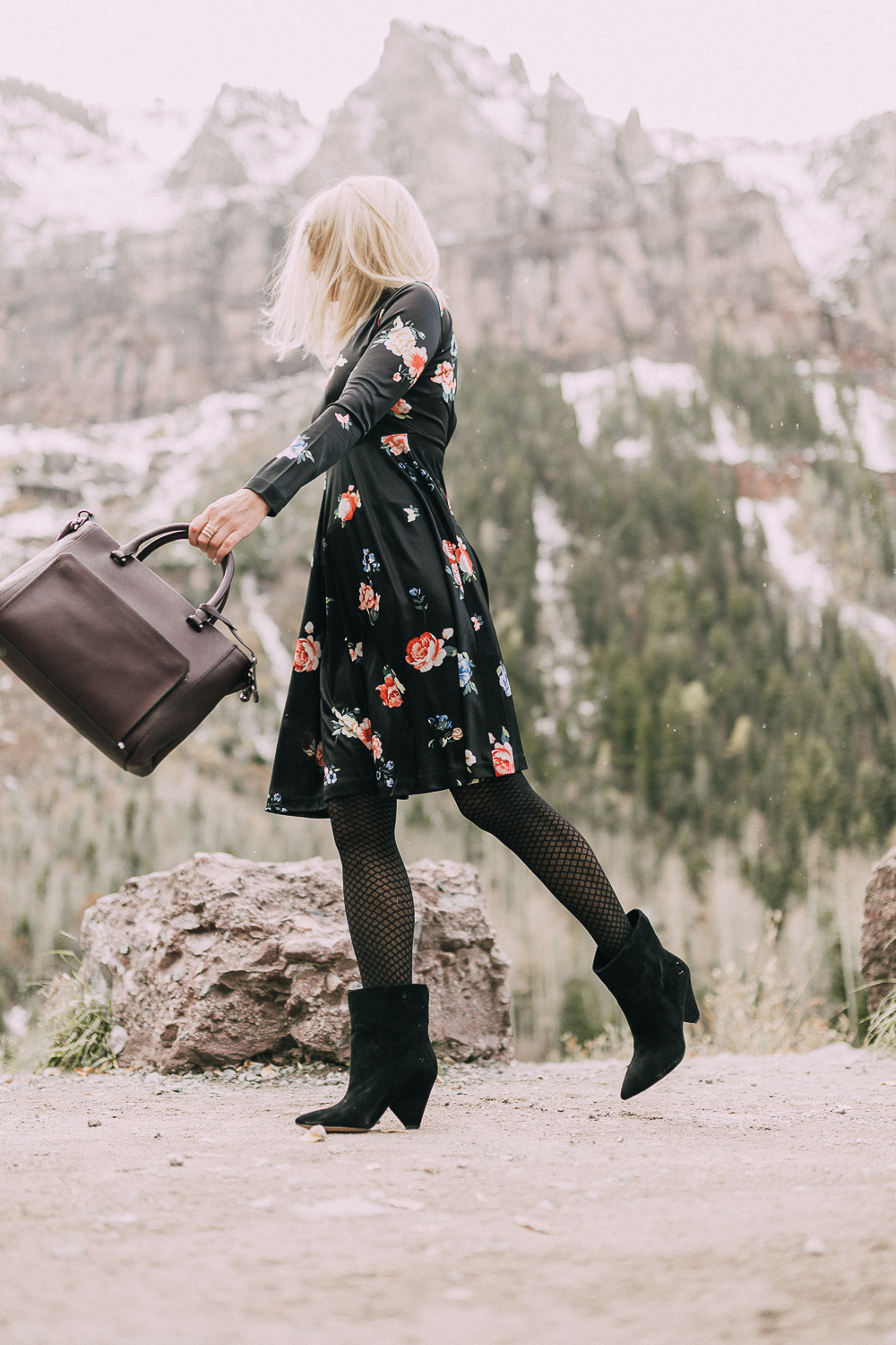 black regina Suede Booties by Vince Camuto paired with black floral print dress and leather burgundy tote bag on blonde woman in rocky mountains