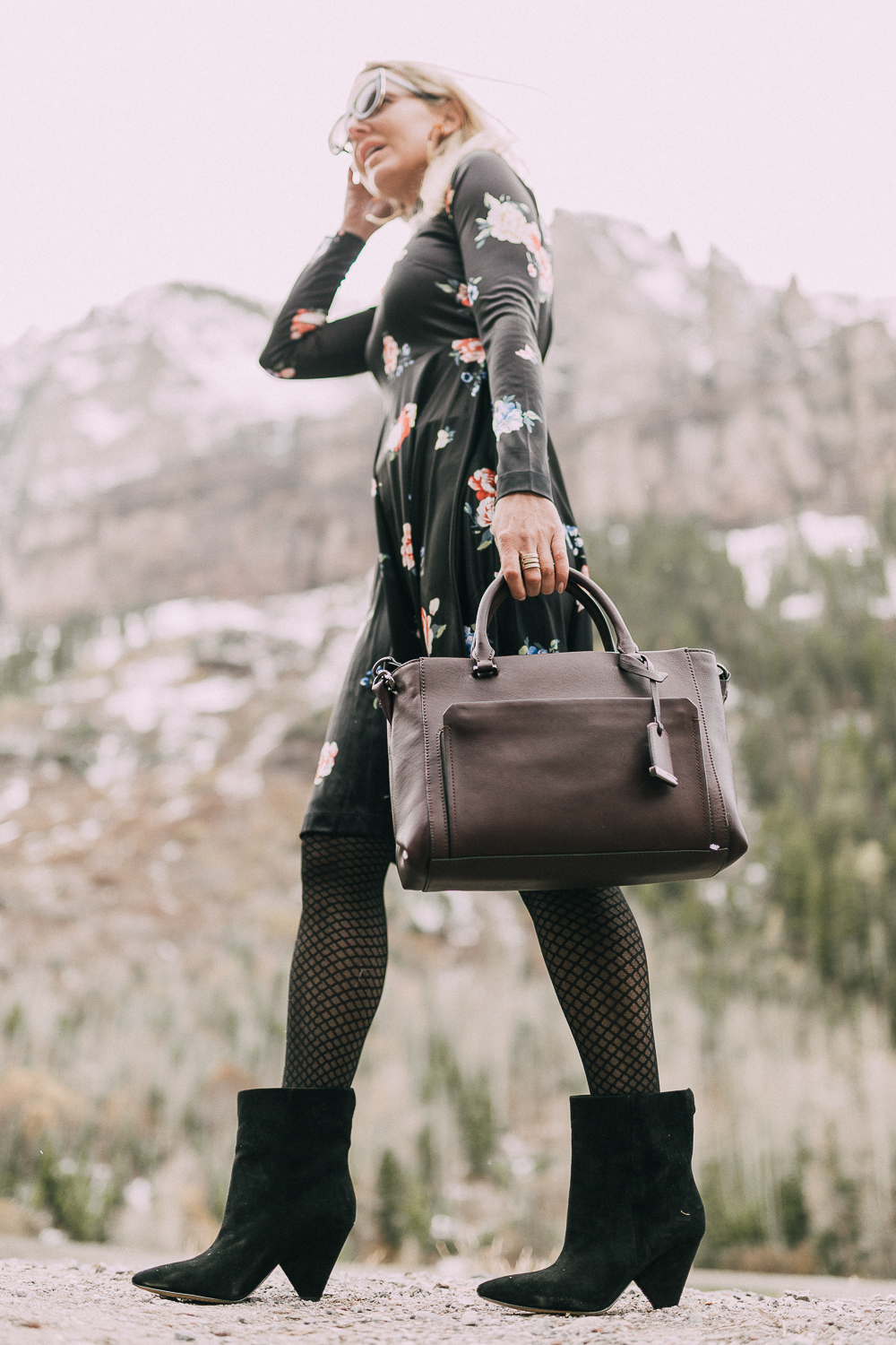 black regina suede ankle booties by Vince Camuto worn with black floral print dress and burgundy tote bag on blonde woman in rocky mountains